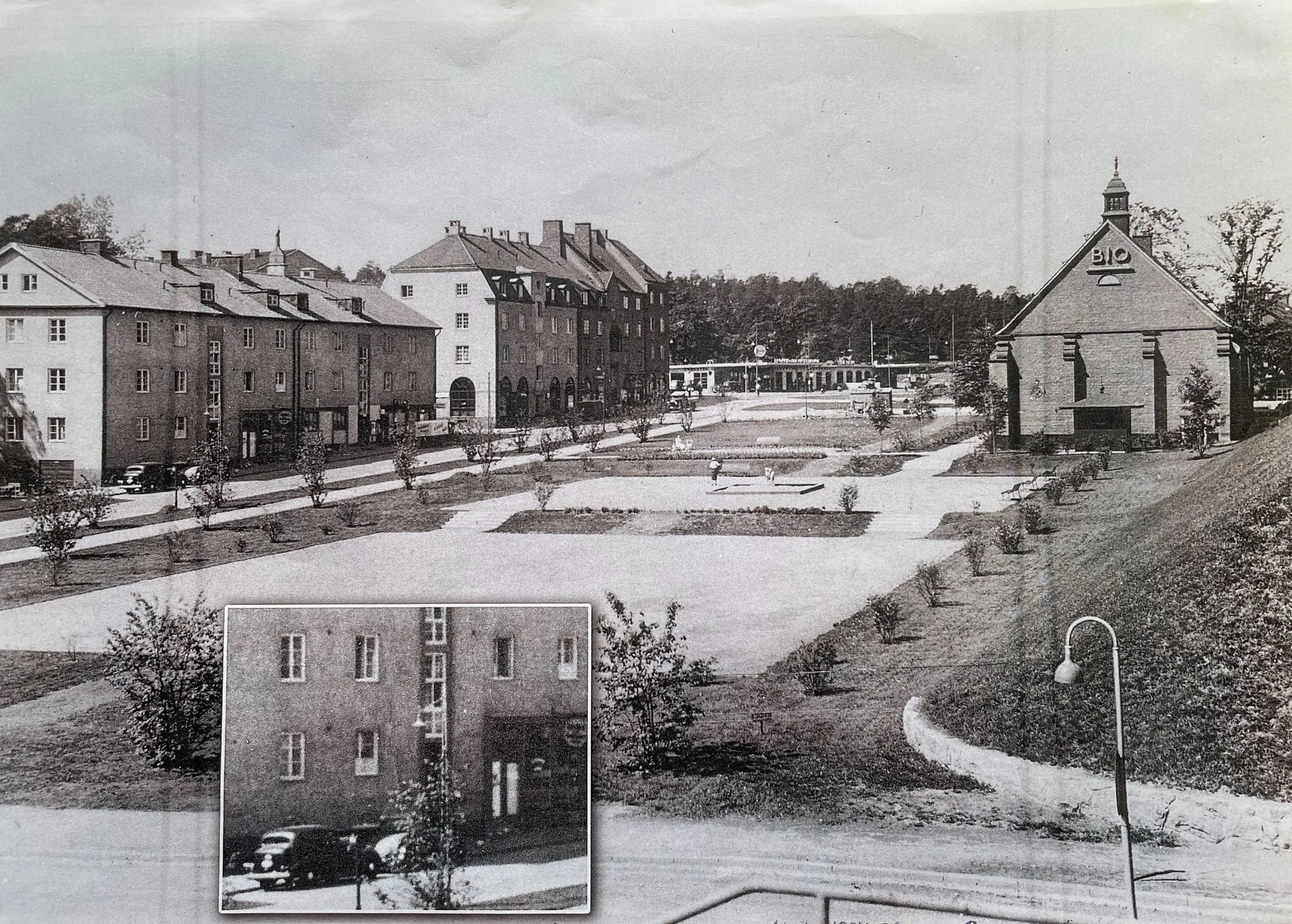 En svartvit bild av ett torg med flera äldre byggnader, ett biorum med skylt riktad mot gatan, och ett fastighetshus med många fönster, samt några träd och ett par bilar.