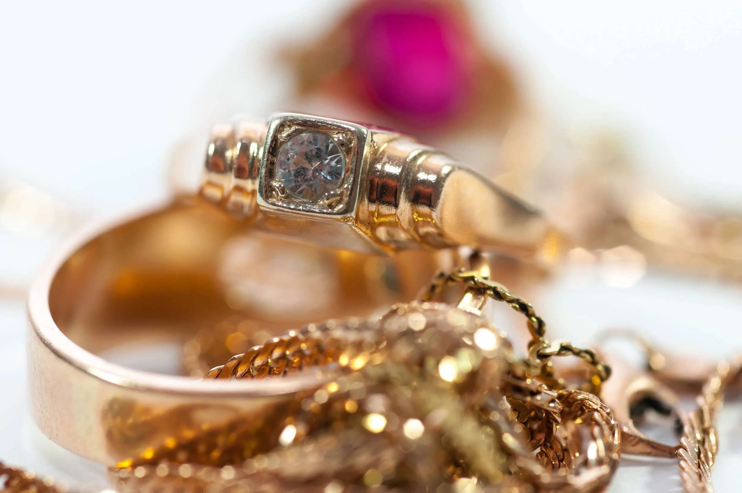 Close-up of a gold ring with a central diamond and gold chains behind it.