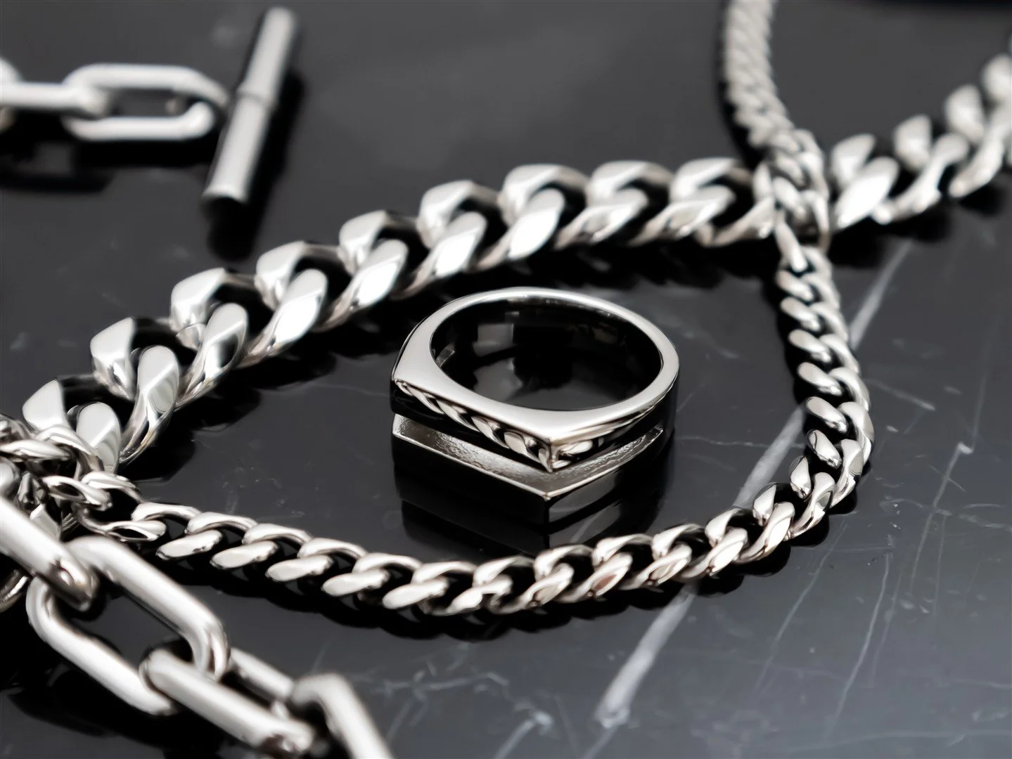 Close-up of a silver chain necklace with a large ring-shaped pendant on a dark surface.
