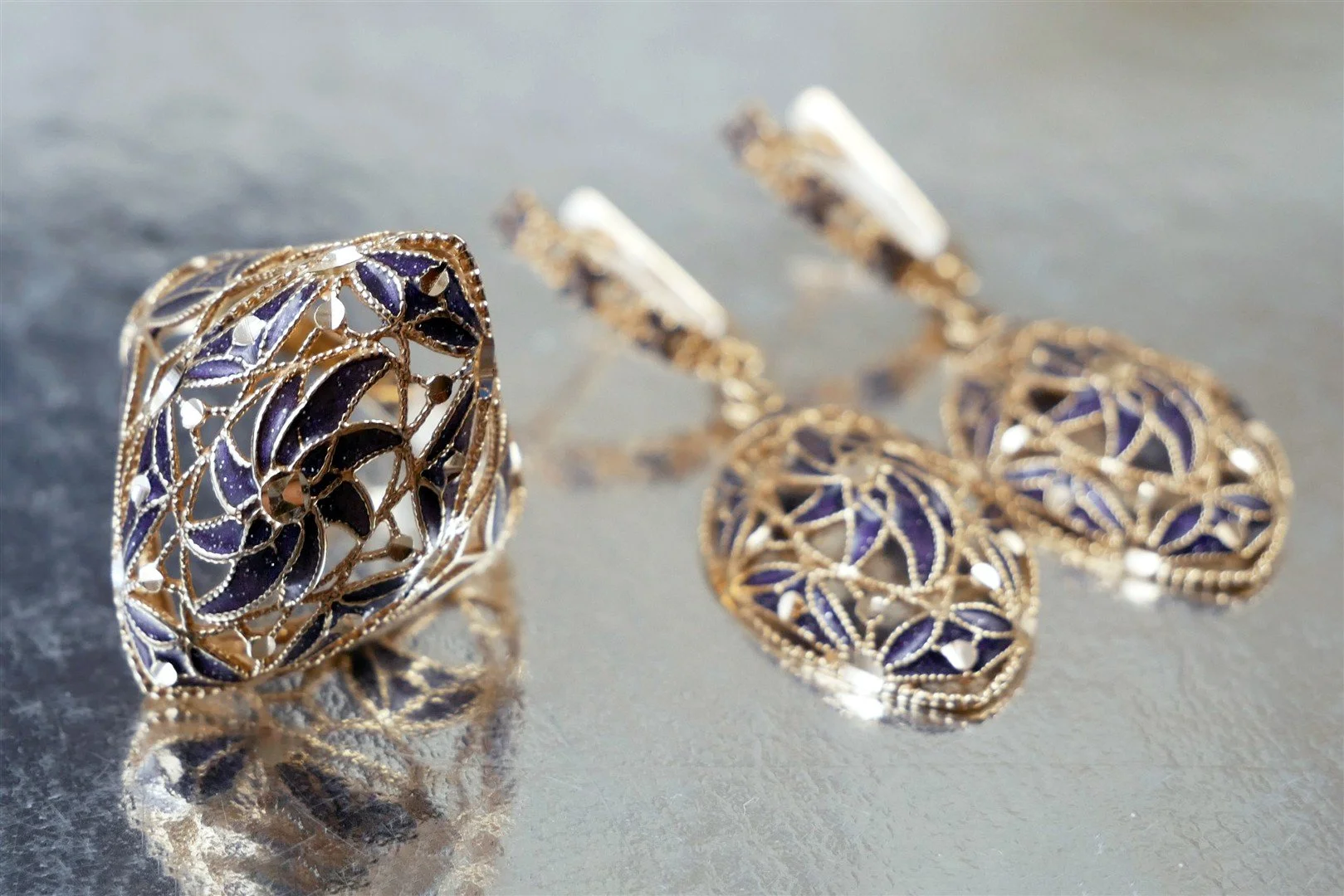 Gold jewelry set consisting of a ring and matching earrings with purple and clear gemstones on a reflective surface.