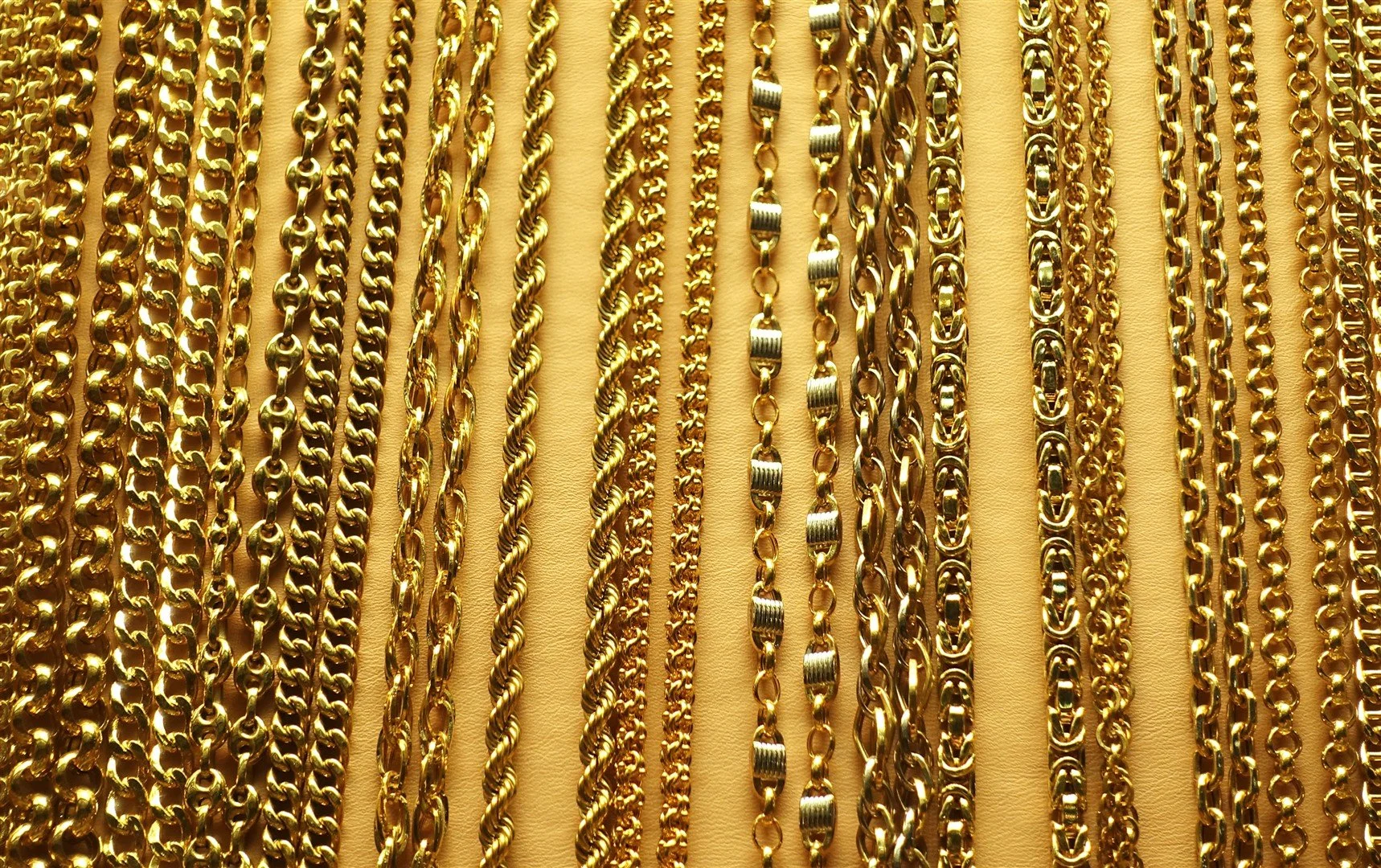 Various gold chains with different link styles hanging against a beige background.