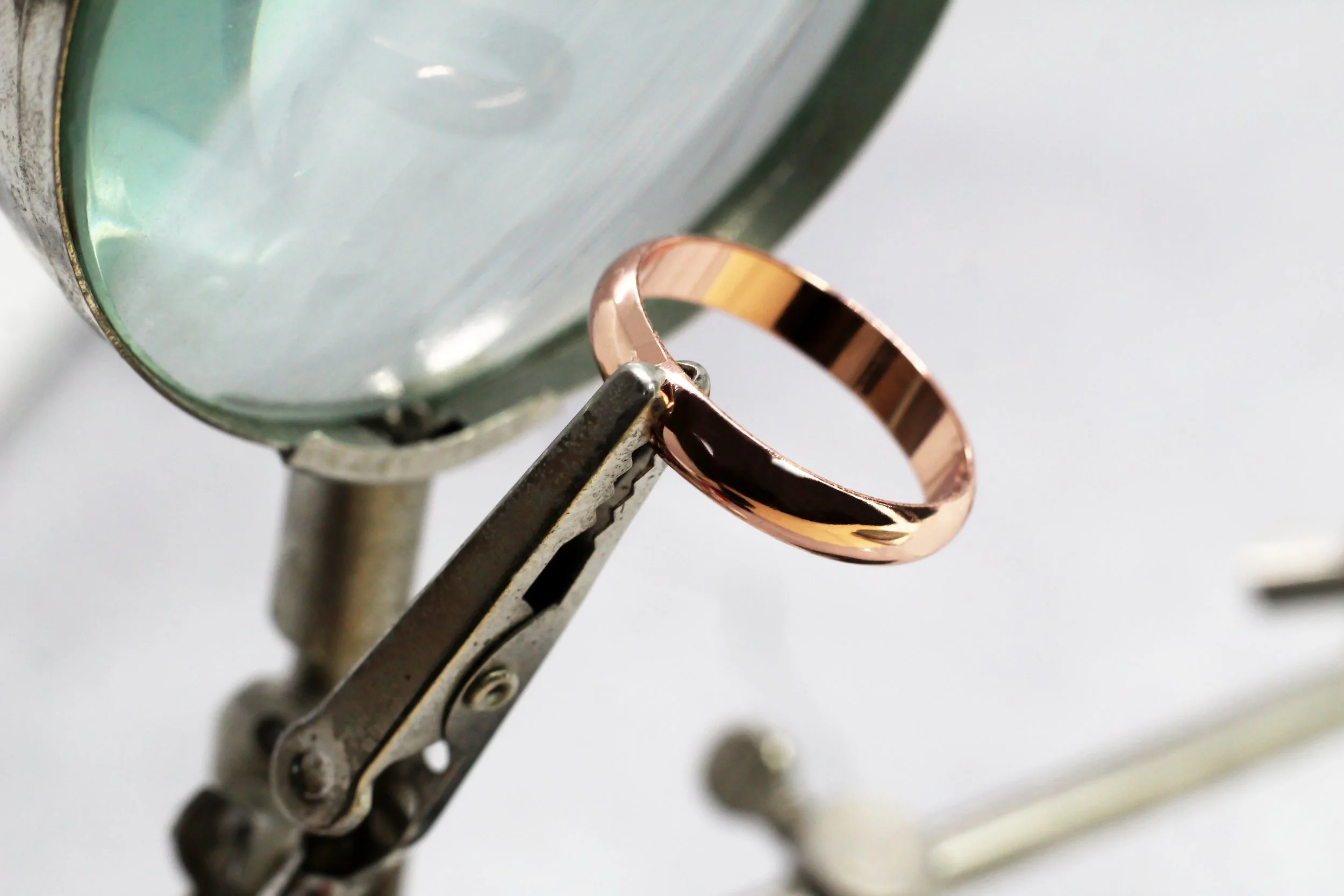 A close-up photo of a rose gold ring resting on a metallic surface, with a blurred background.