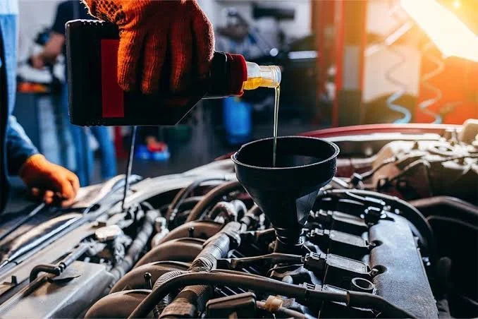 A person wearing a red glove pouring oil into a car engine.