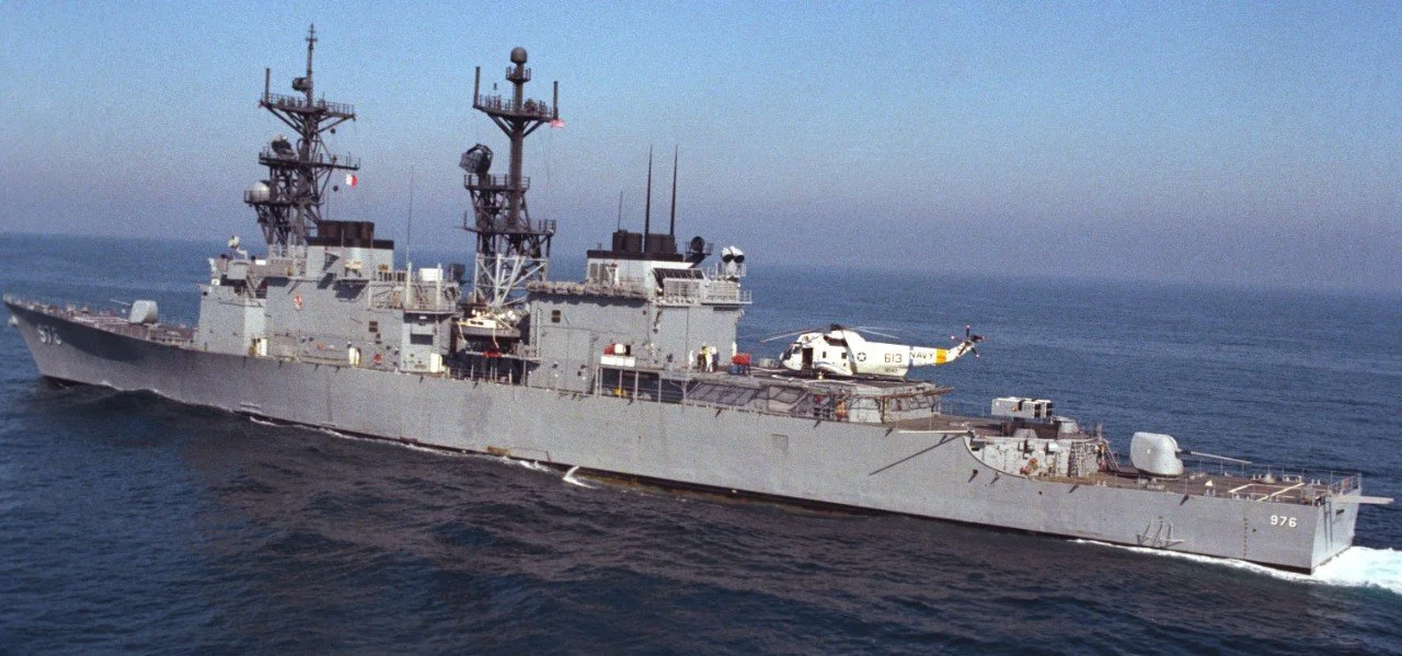 Military ship with two radar towers and a helicopter on the deck.