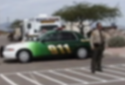 A police officer standing in front of a green and white police car in a parking lot.