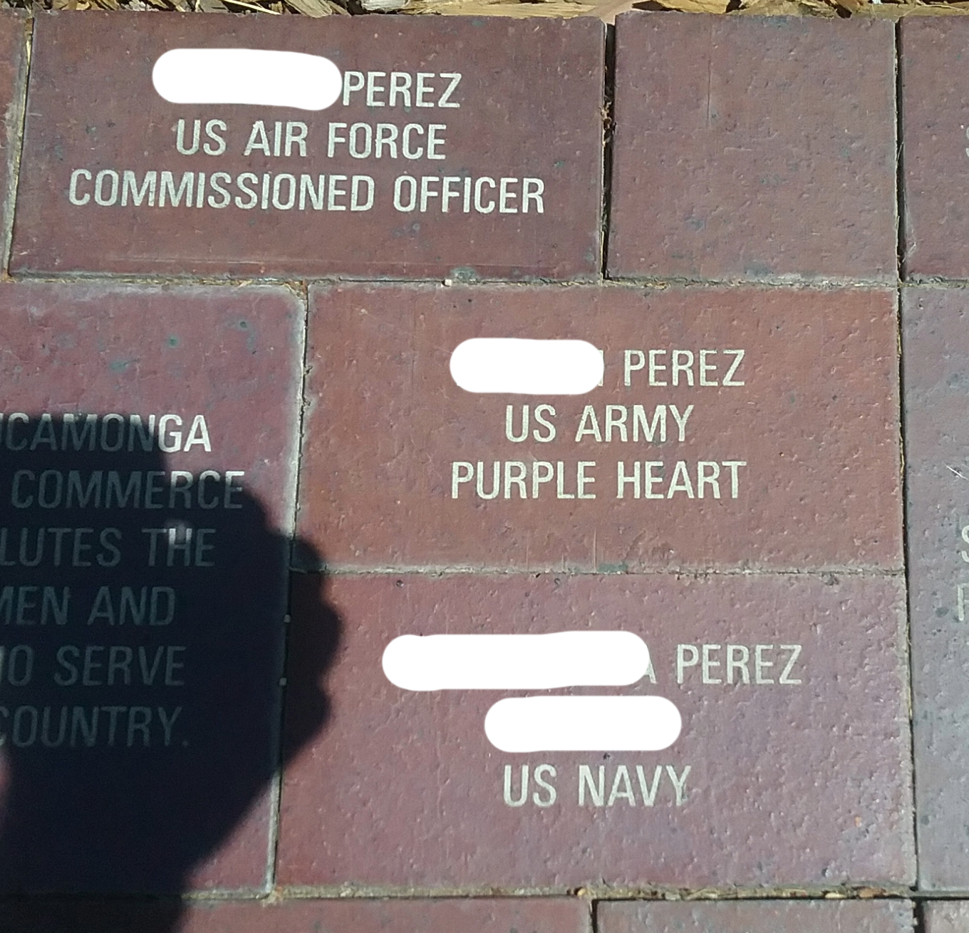 Brick sidewalk with engraved plaques honoring military personnel, including a US Air Force officer, a US Army member with a purple heart, and a US Navy member, all with the surname Perez.