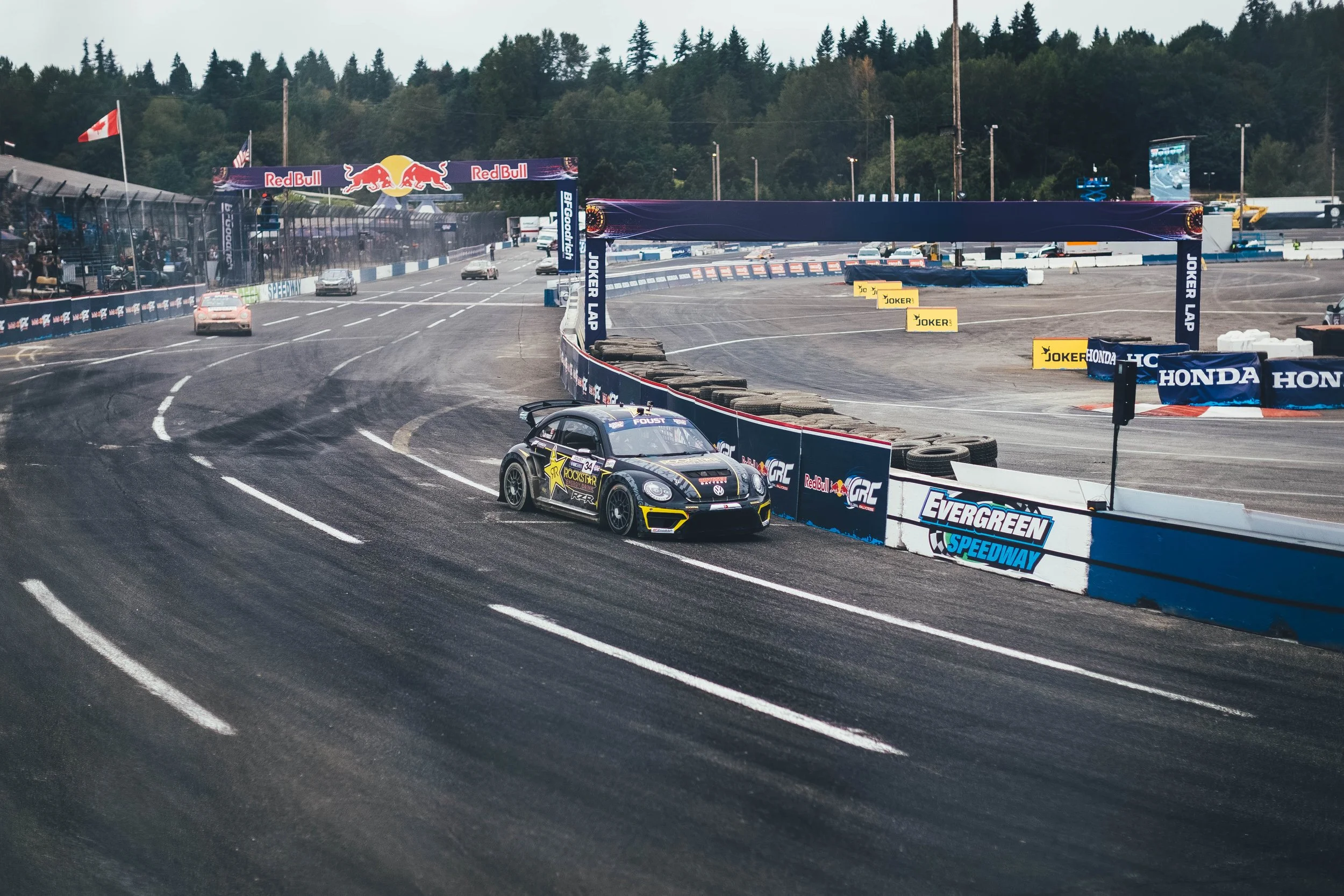 A race car on a racing track during a motorsport event with sponsor banners and spectators in the stands.