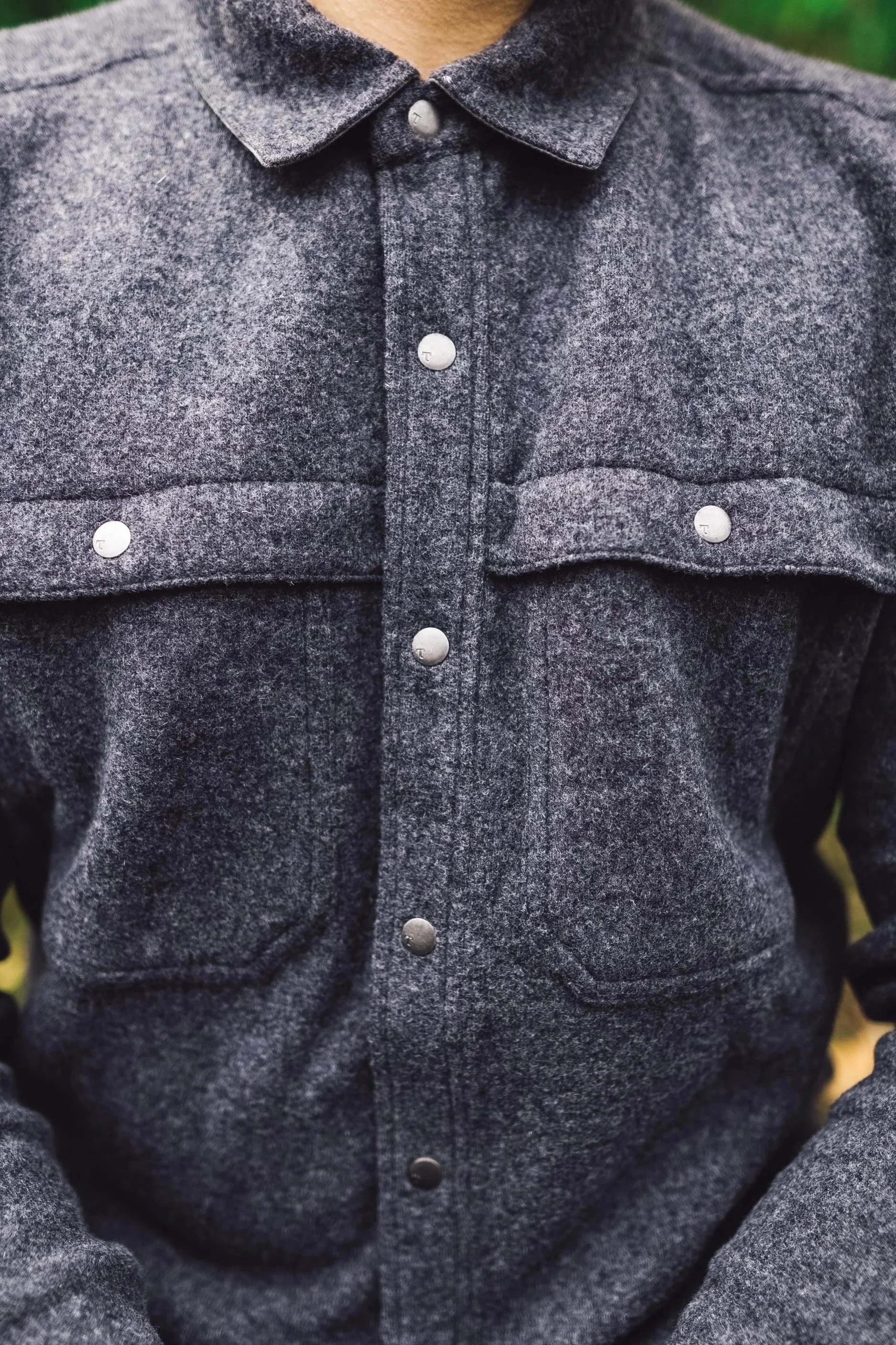 Close-up of a dark grey, flannel shirt with silver snaps and a buttoned flap pocket on the chest.