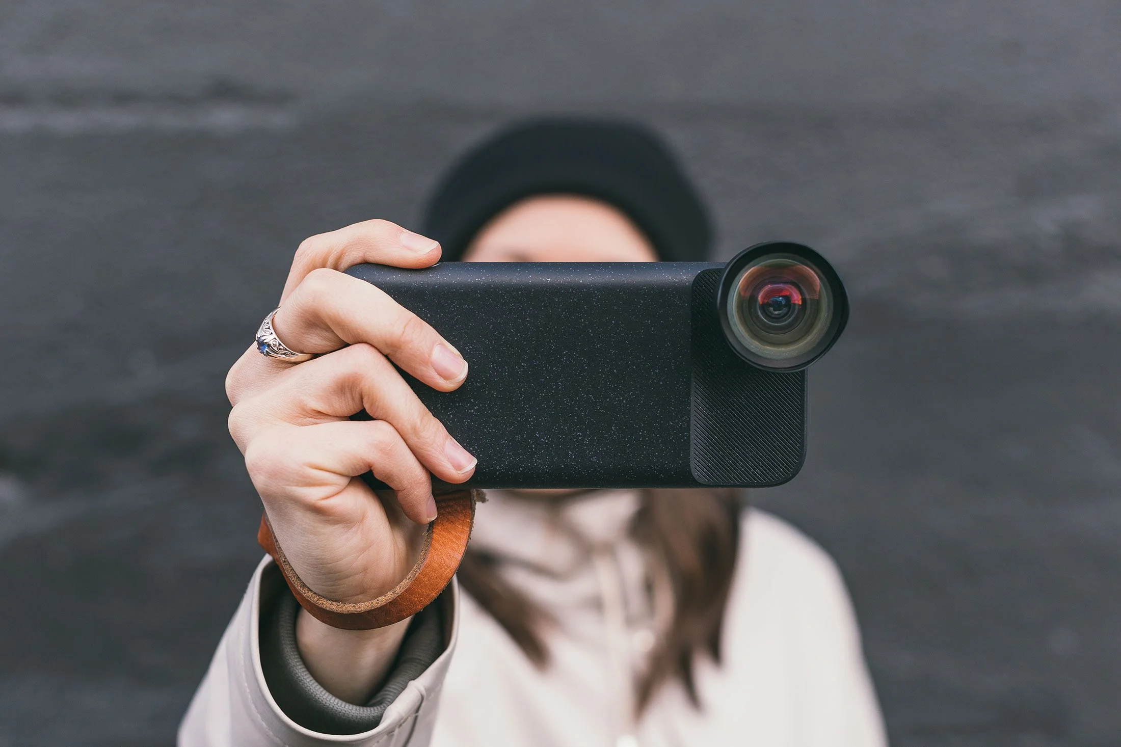 Person holding a smartphone fitted with an external Moment camera lens.