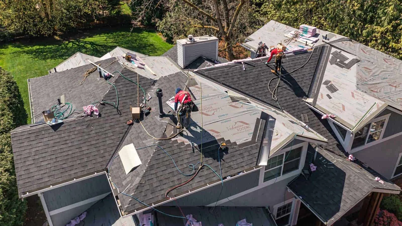 Construction workers repairing or installing a roof on a residential house, with some areas covered in new roofing material and others under preparation.