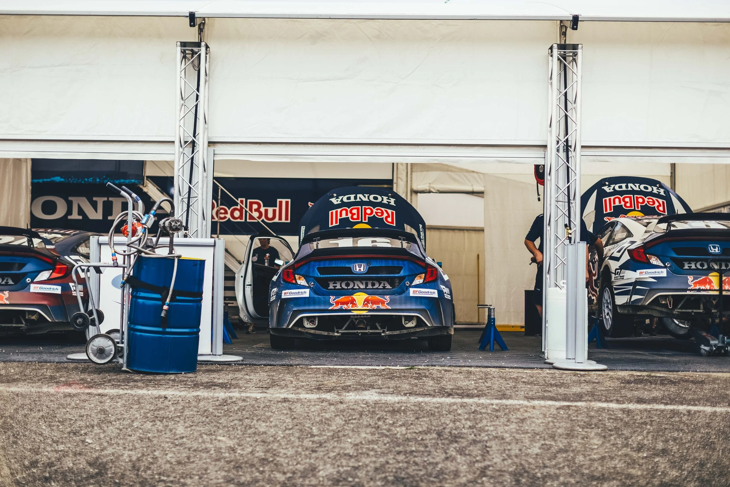 Race cars in a pit garage with Red Bull and Honda logos, and mechanics working around them.