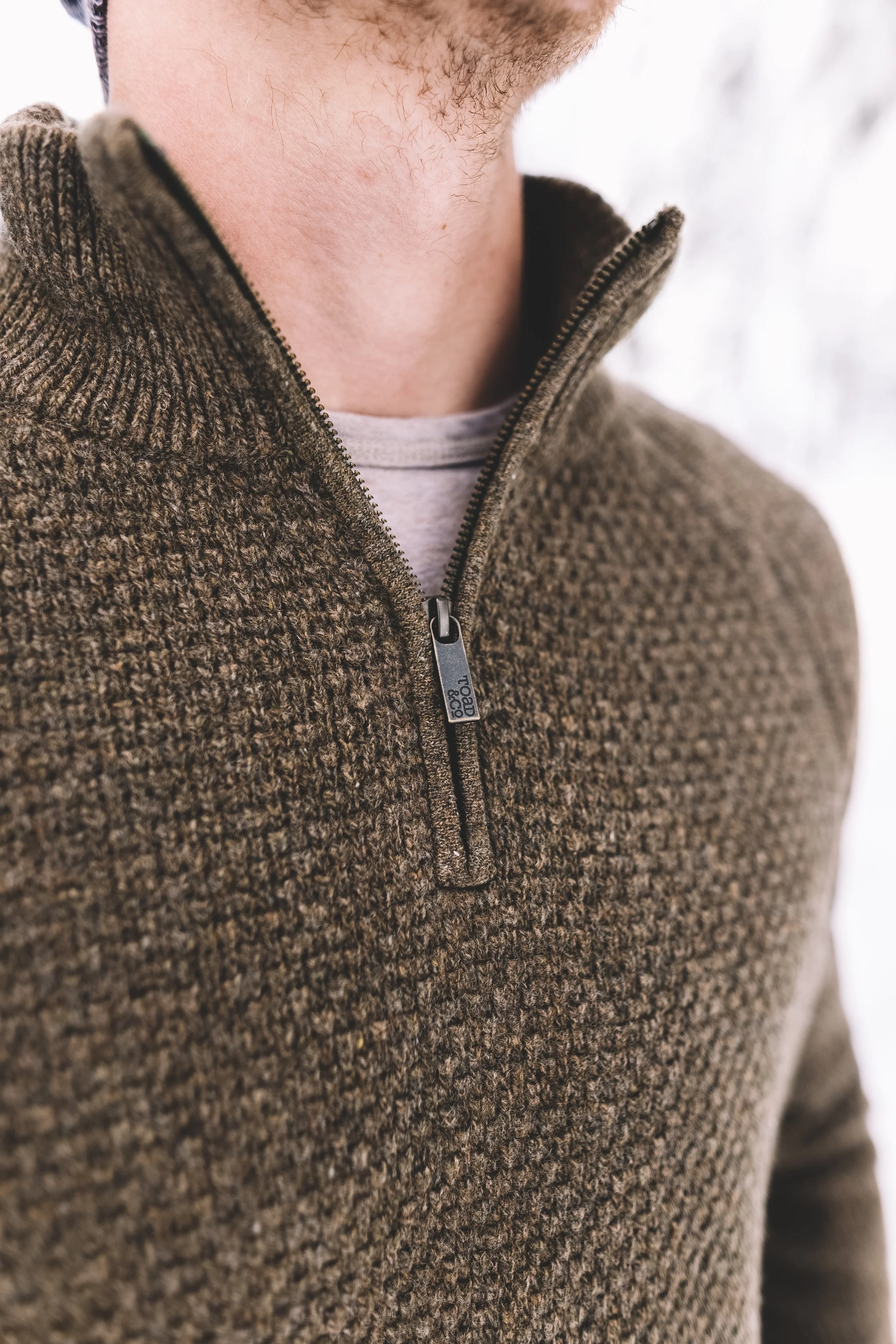 Close-up of a person wearing a brown textured zip-up sweater with a stand-up collar, over a white shirt.