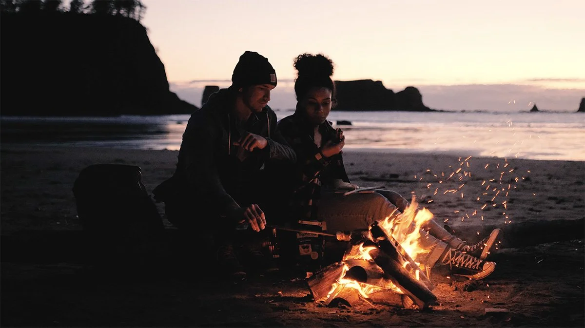 Campers gathered around a beach fire at dusk during production for Aasgard.