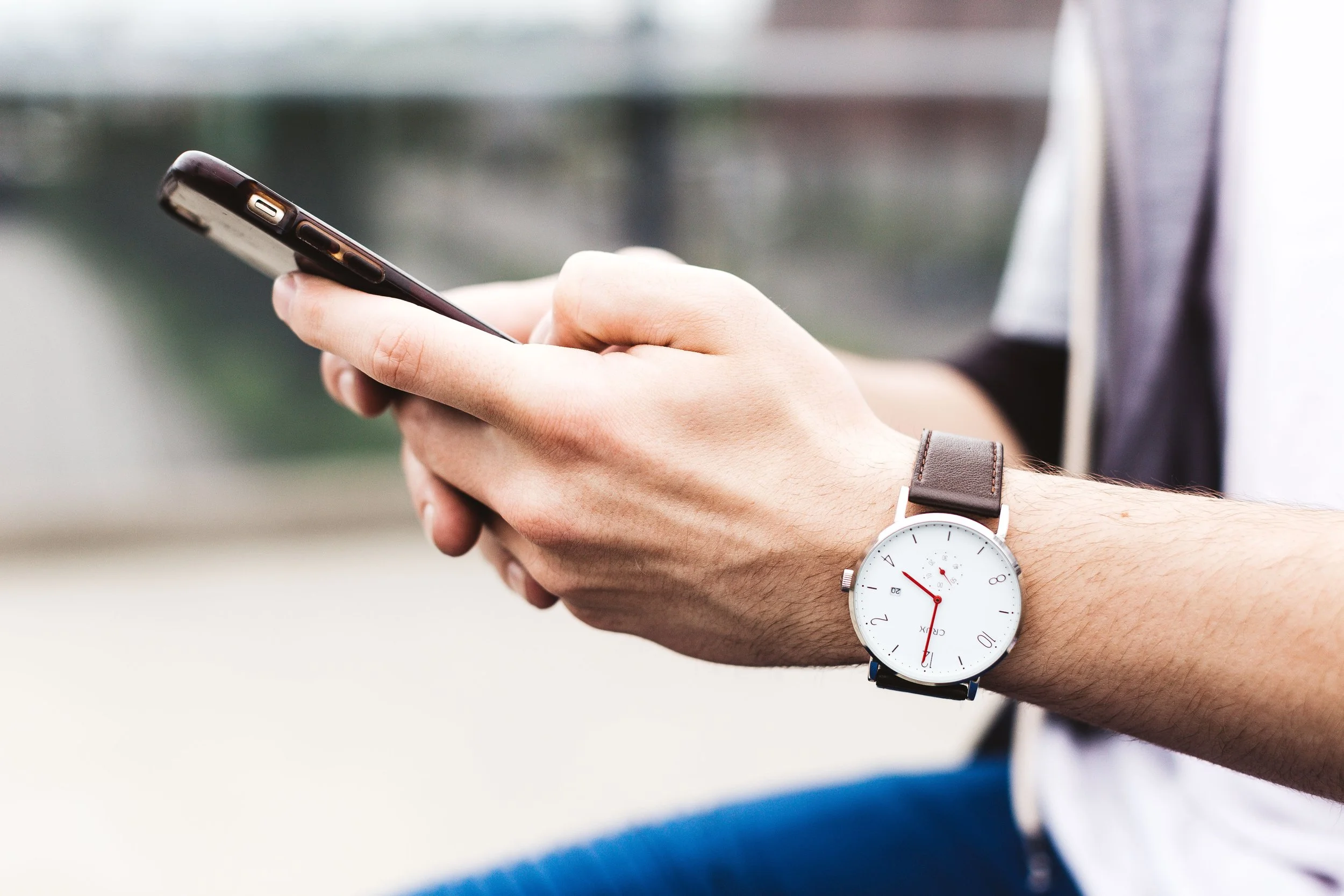 Close-up of a person's hand holding a smartphone, wearing a wristwatch with a white face and black strap.