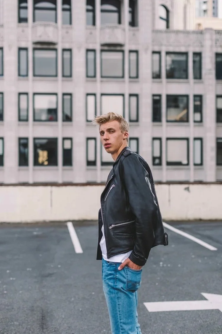 Portrait of a young man in a black leather jacket against an urban building.