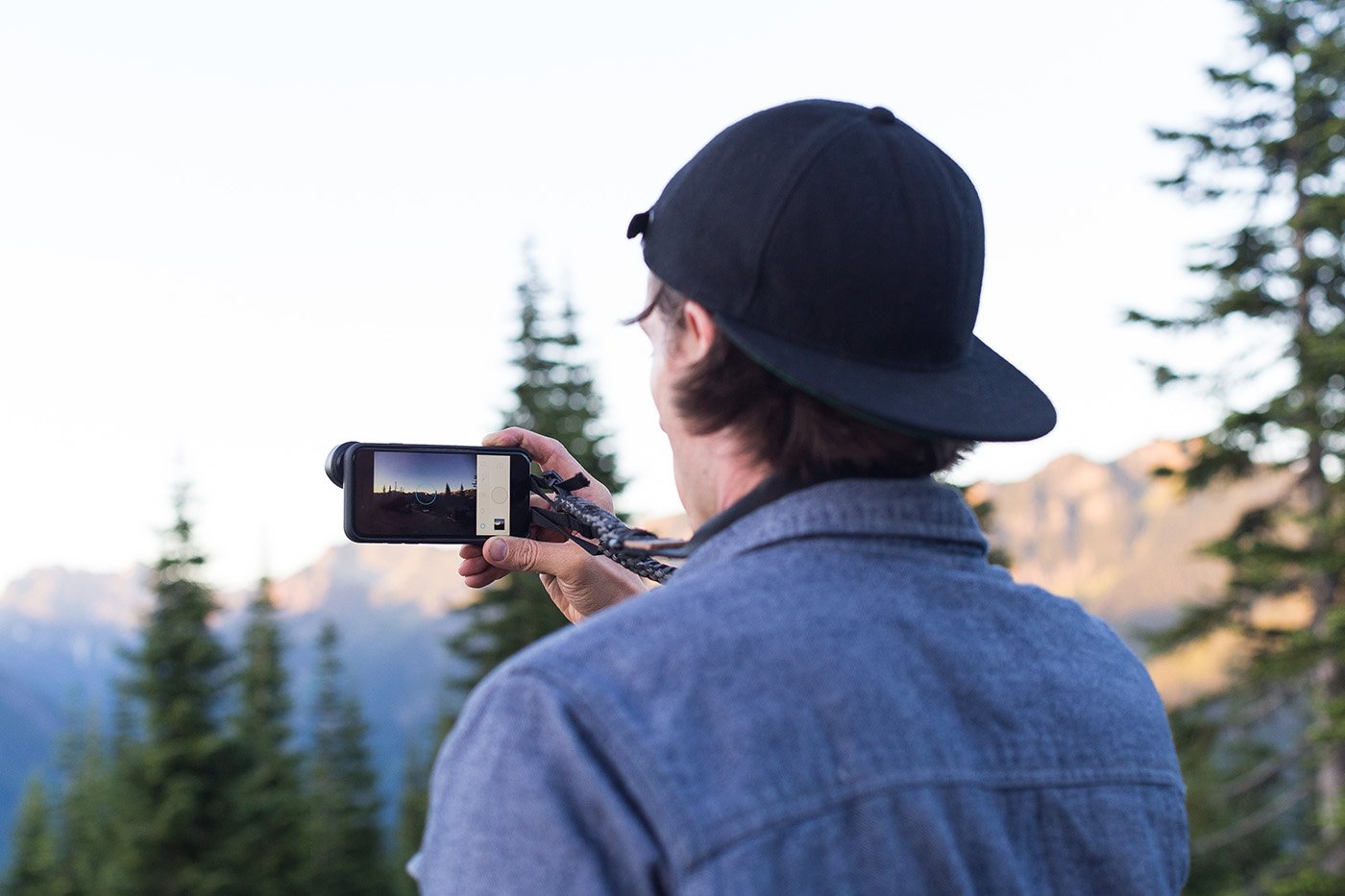 Man photographing a mountain landscape with a smartphone fitted with a Moment lens.