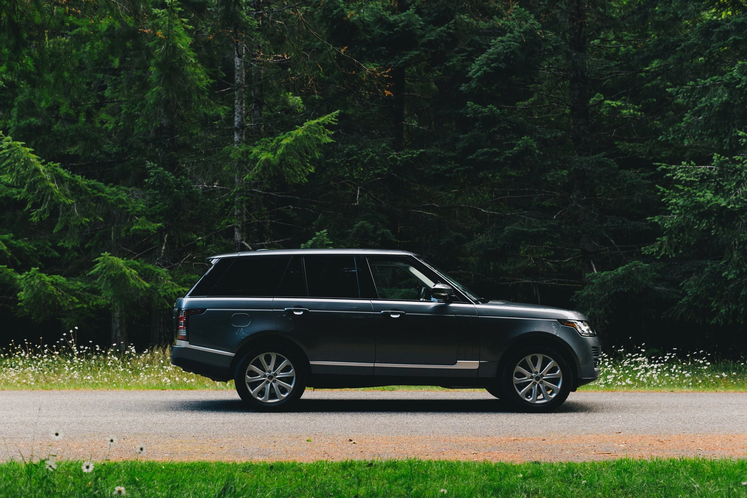 A black Range Rover parked on a road in front of dense green forest trees.