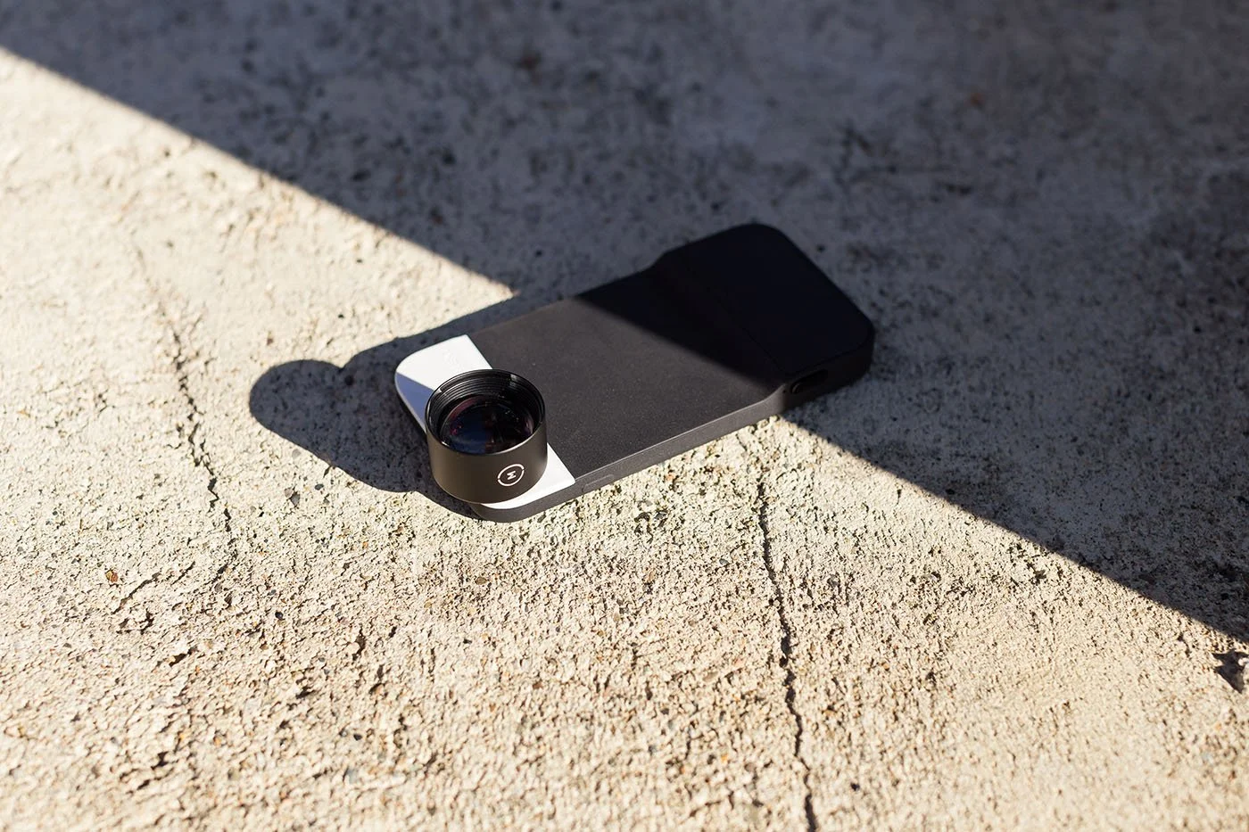 Smartphone with a Moment camera lens resting on sunlit concrete.