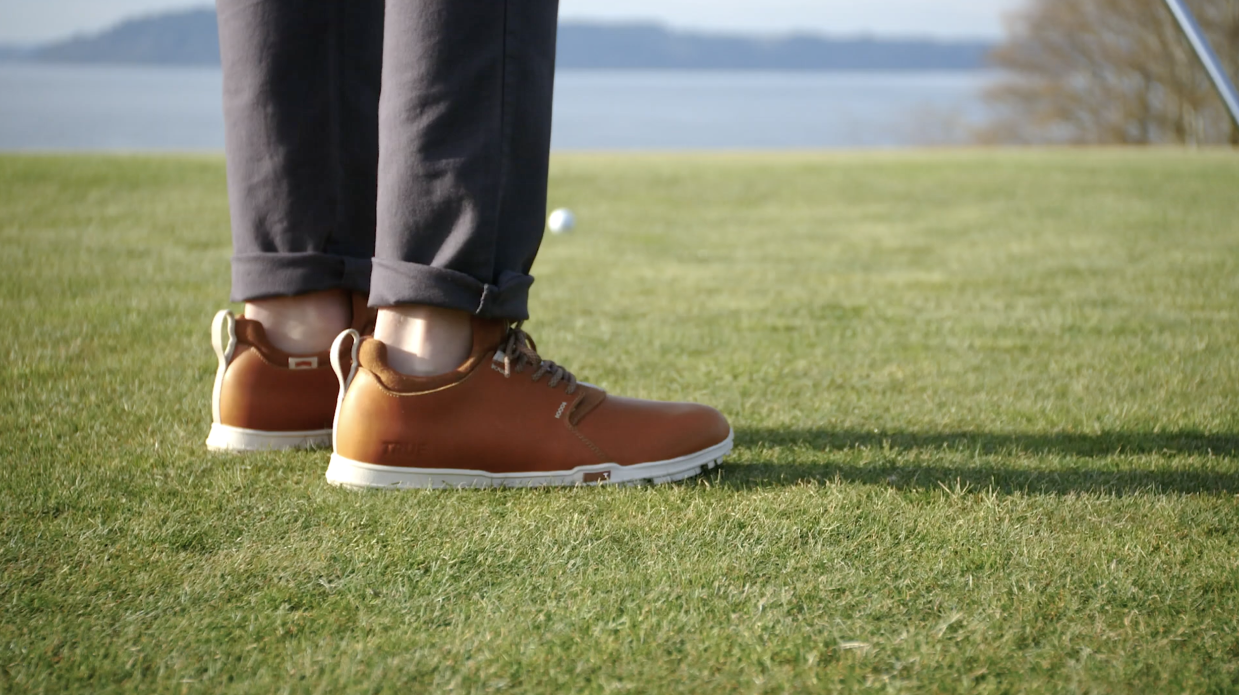 Brown TRUE Linkswear golf shoes worn on a green fairway.