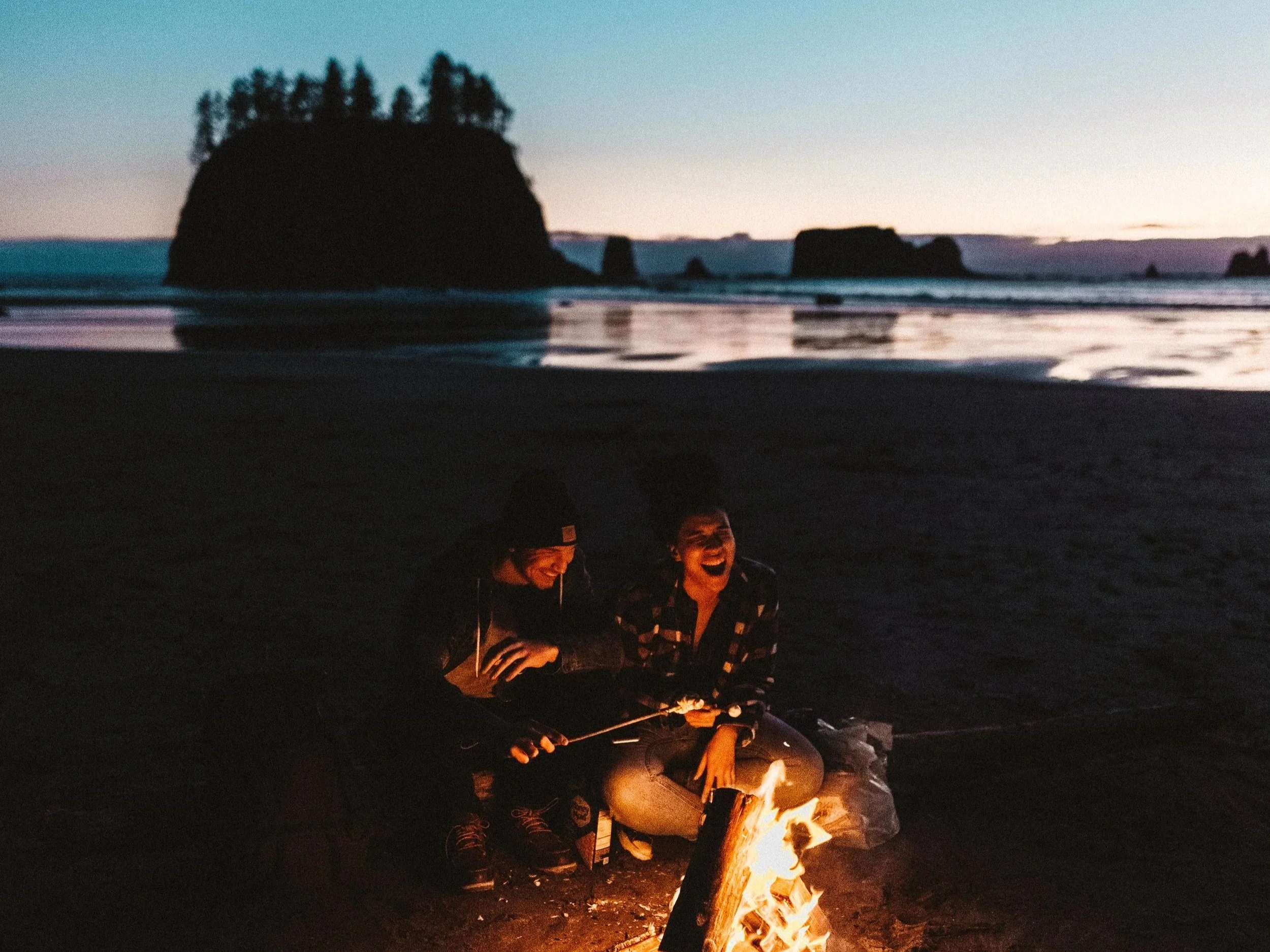 Campers gathered around a fire on a beach at dusk for Aasgard.