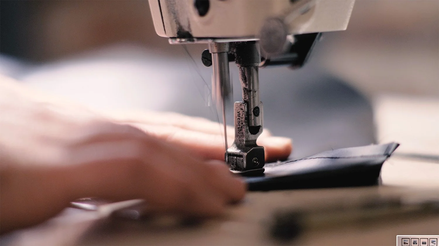 Close-up of hands guiding gray backpack fabric beneath an industrial sewing machine needle.