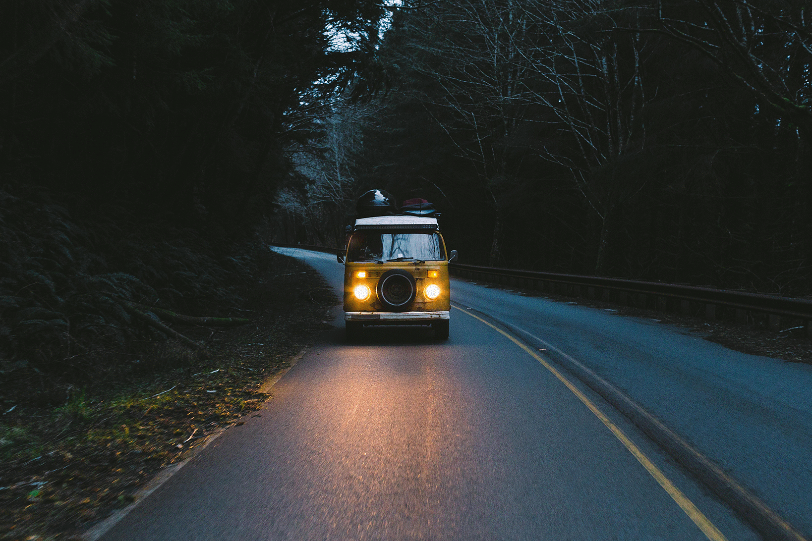 Vehicle driving at night on a forest road with its headlights on.