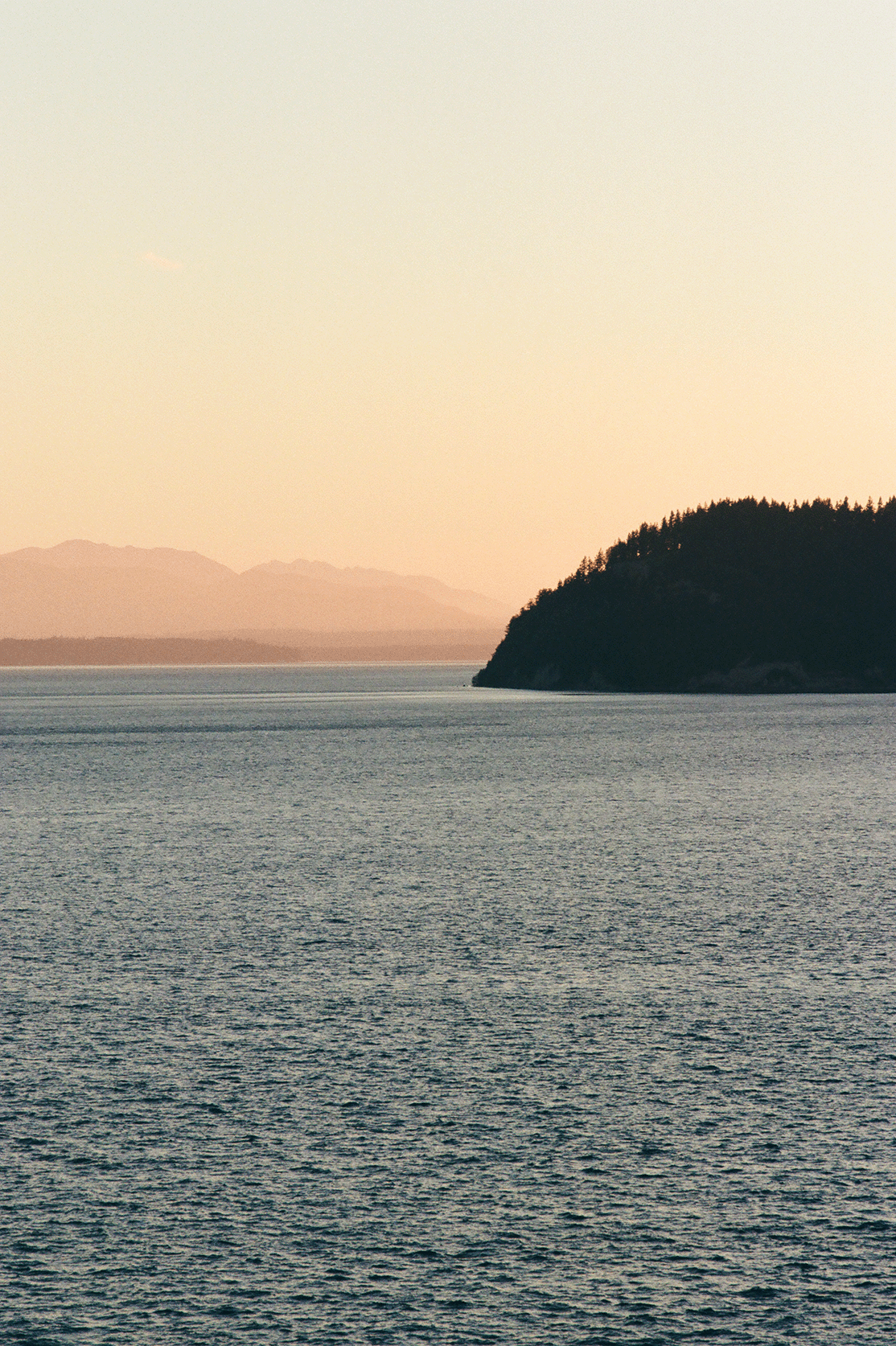 Whidbey island silhouetted across calm water at dusk.