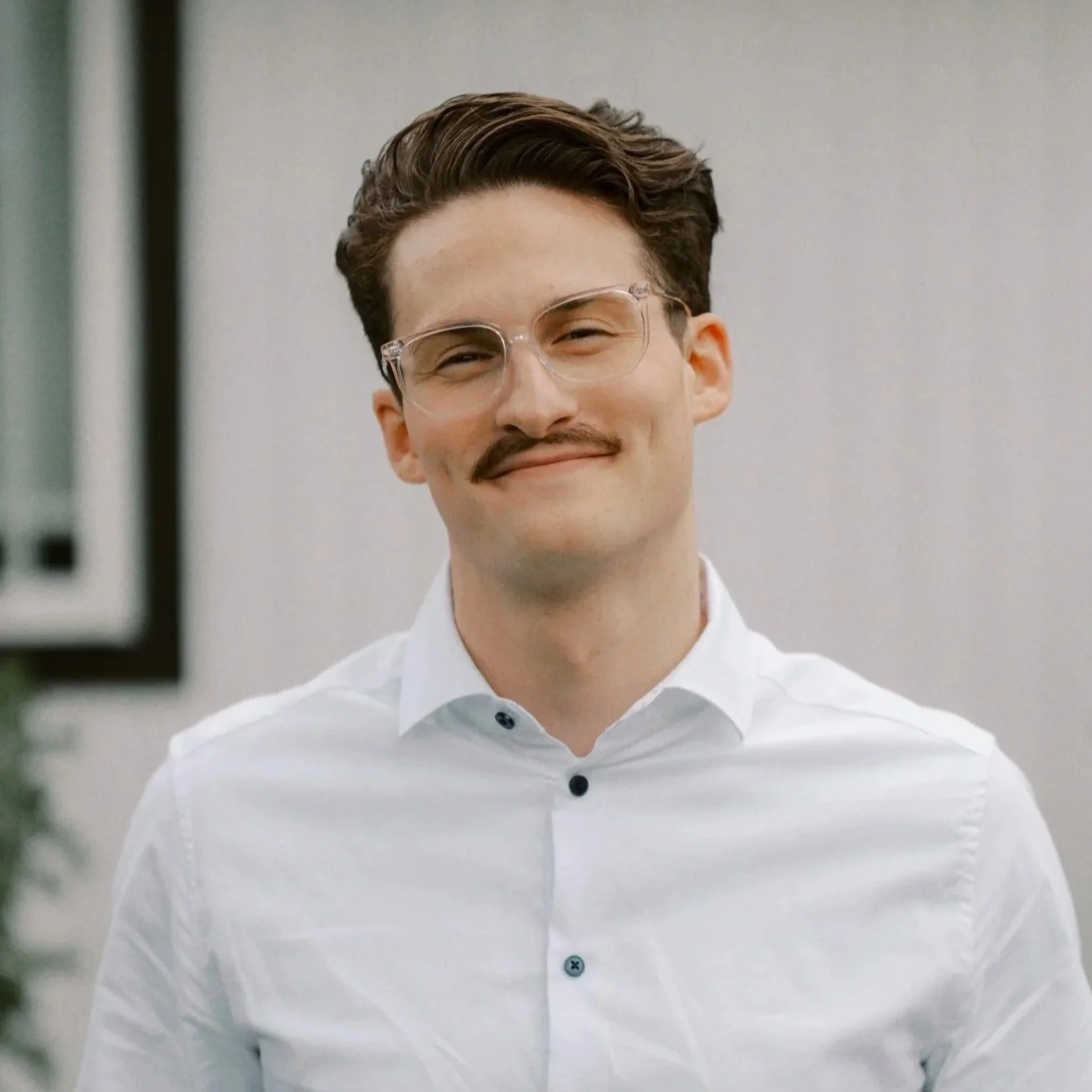Portrait of a man wearing clear-frame glasses and a white collared shirt.