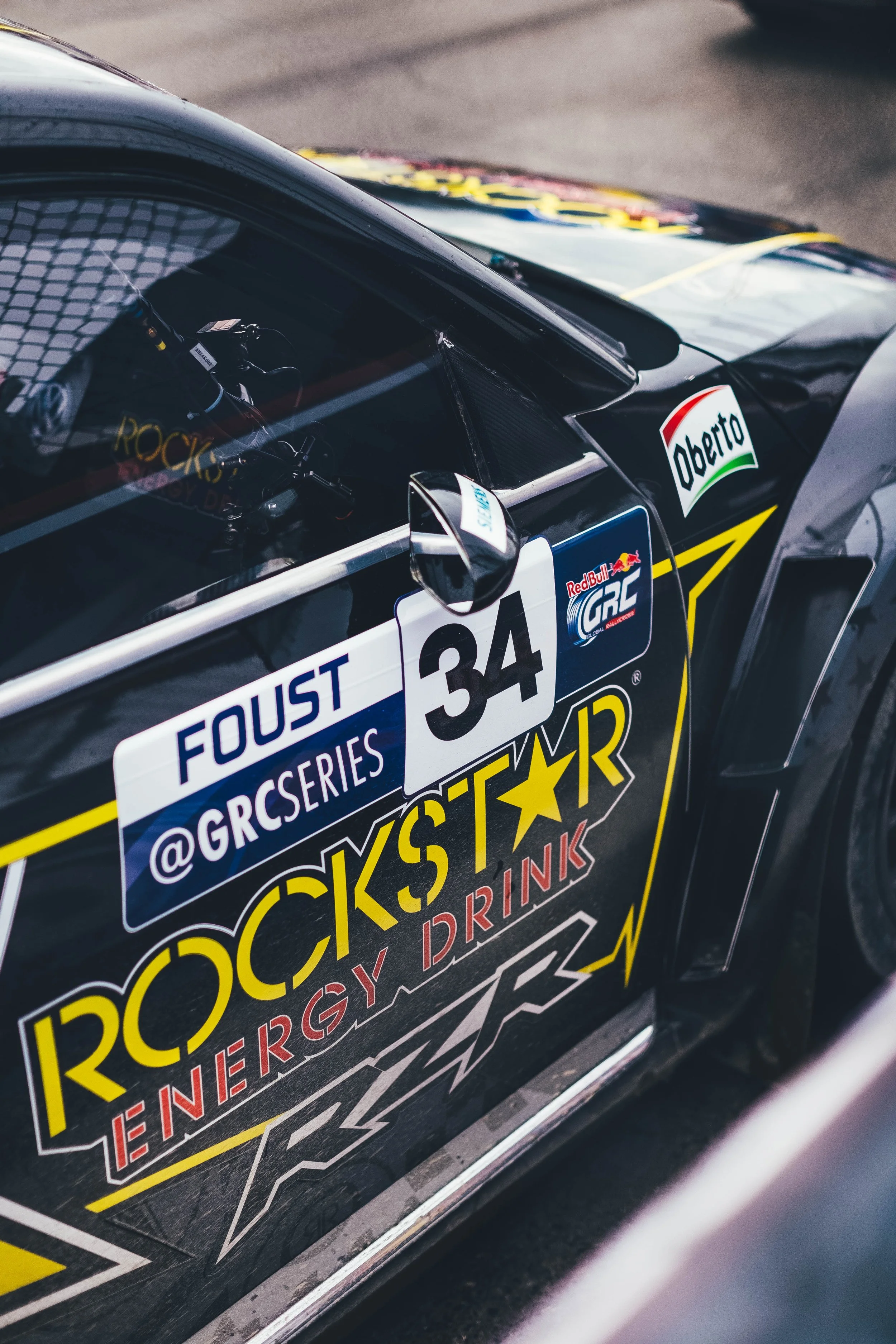 Close-up of a race car with sponsor logos including Rockstar Energy, Oberto, and Red Bull, featuring the number 34 on the door.