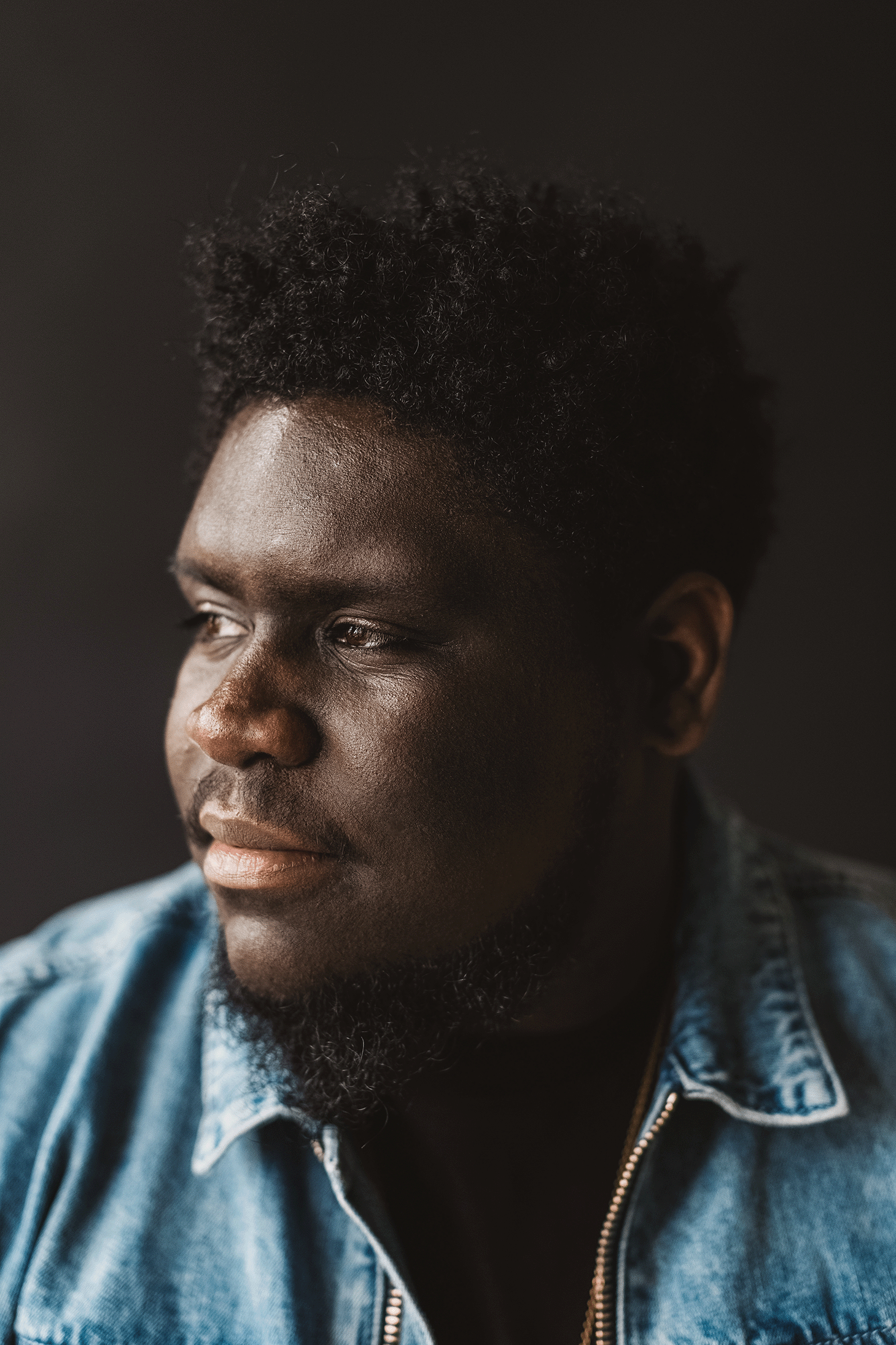 Studio portrait of a man wearing a denim shirt against a neutral backdrop.
