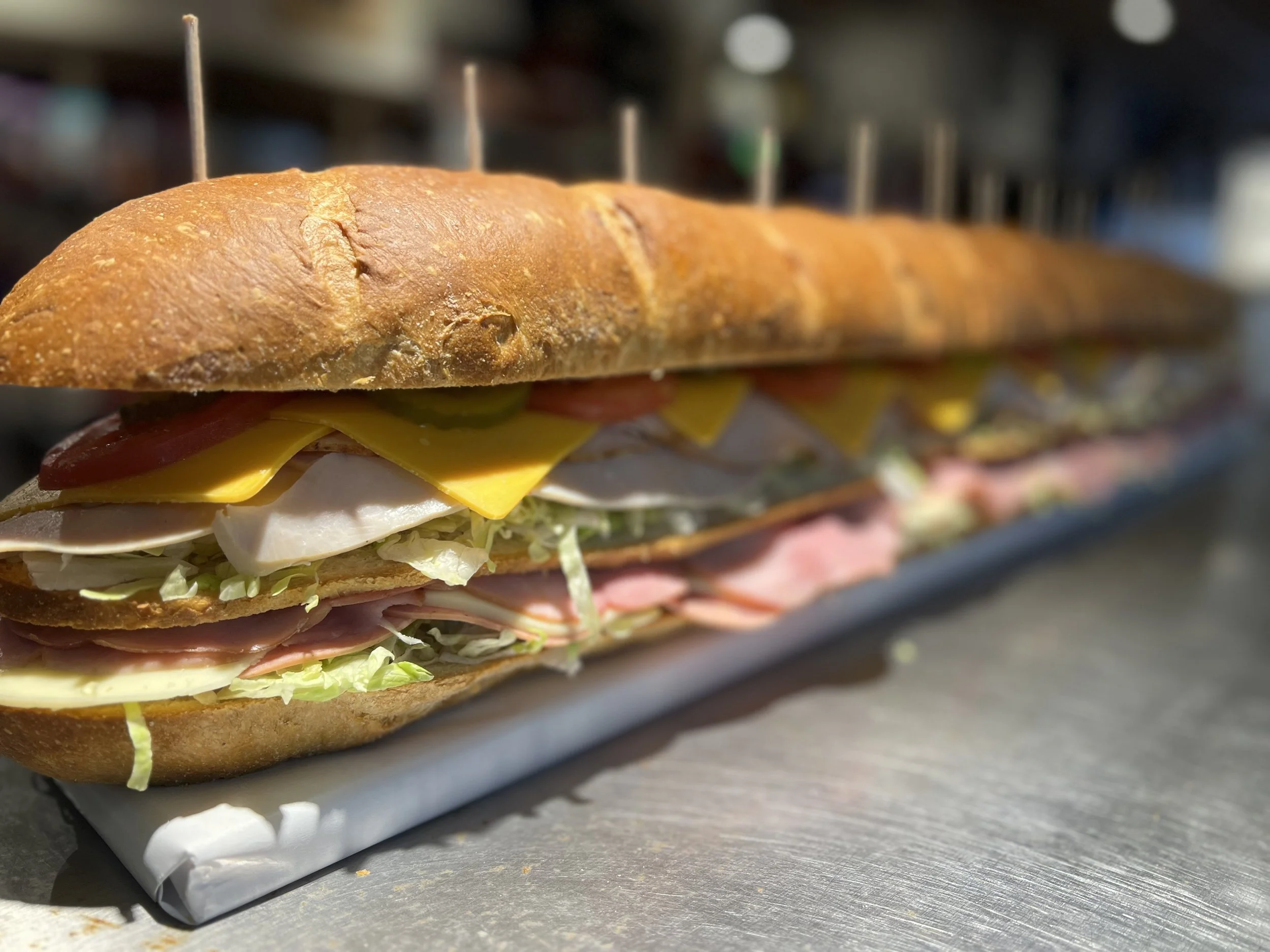 Close-up of a sandwich with a crusty baguette, ham, turkey, cheese, lettuce, tomato, and onion on a tray