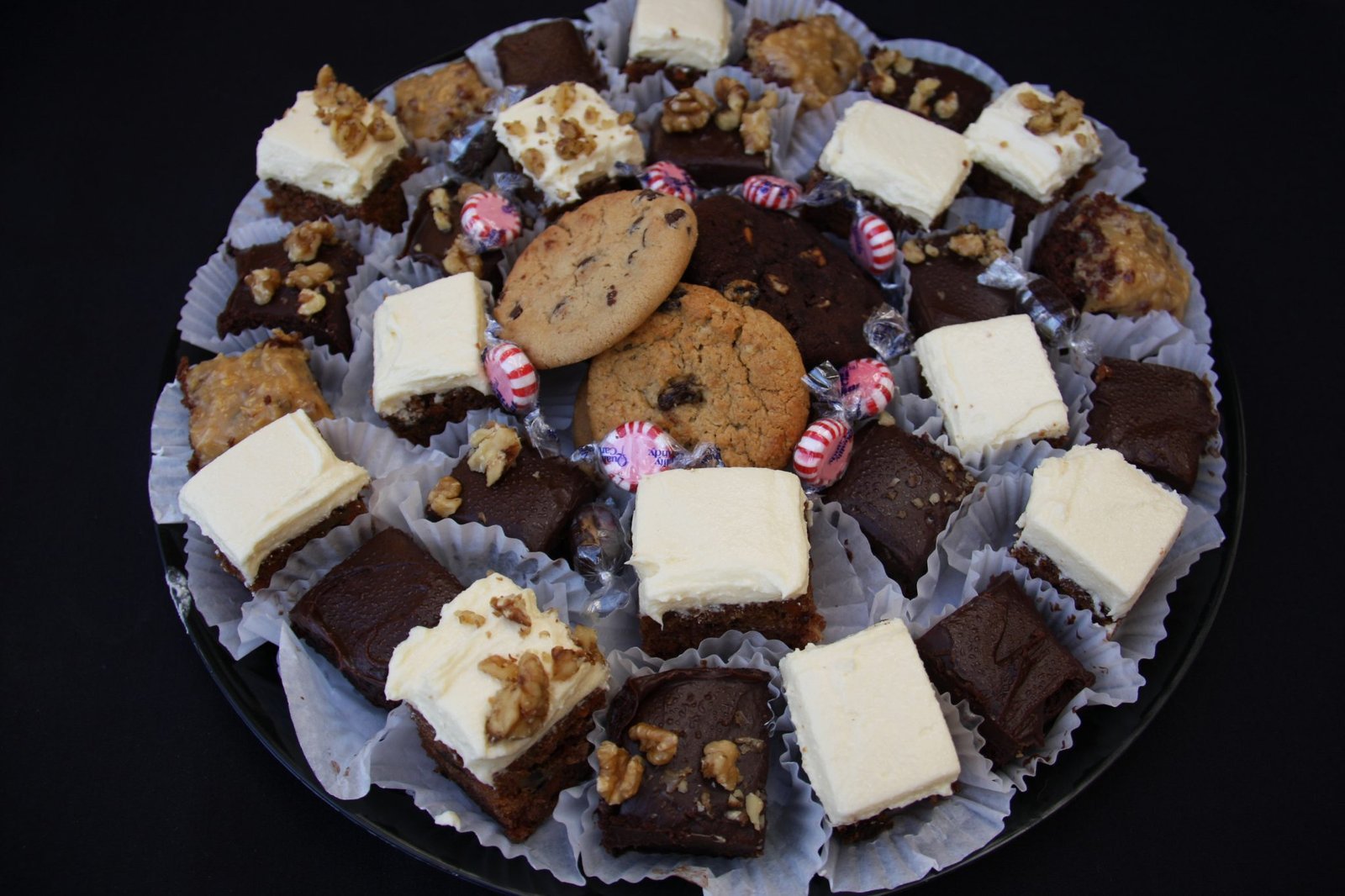Assorted brownies, frosted dessert squares, chocolate chip cookies, walnuts, and peppermint candies on a serving platter