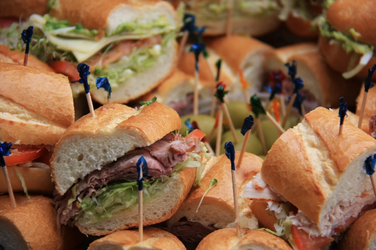 Assorted baguette sandwich appetizers with deli meat, turkey salad, lettuce, tomatoes, and decorative toothpicks