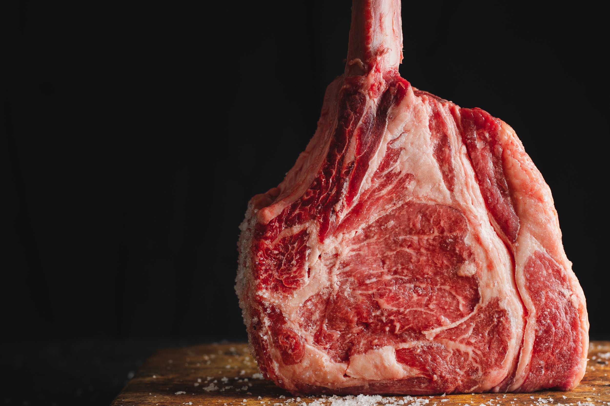 Raw marbled beef roast with coarse salt on a wooden cutting board against a black background