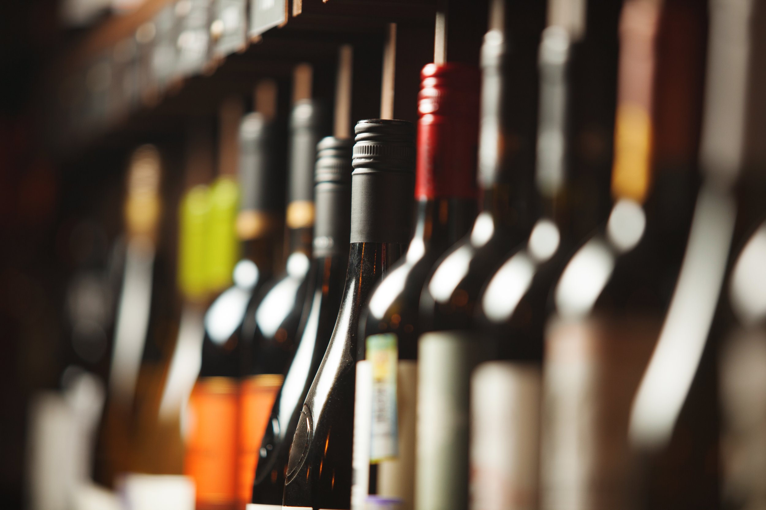 Close-up of colorful wine bottles arranged on a shelf with shallow depth of field