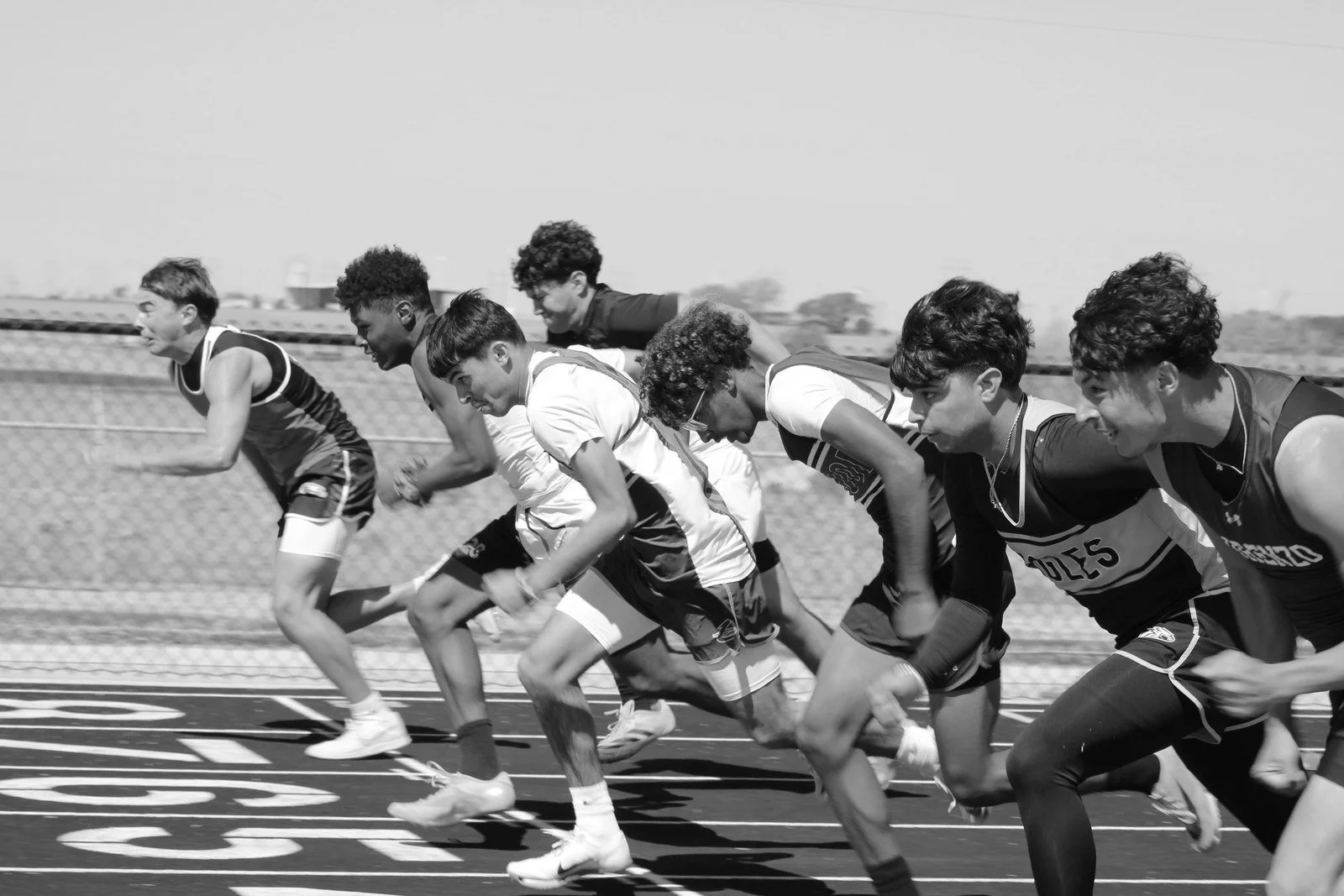 A group of young male athletes at the start of a race on a track, preparing to run.