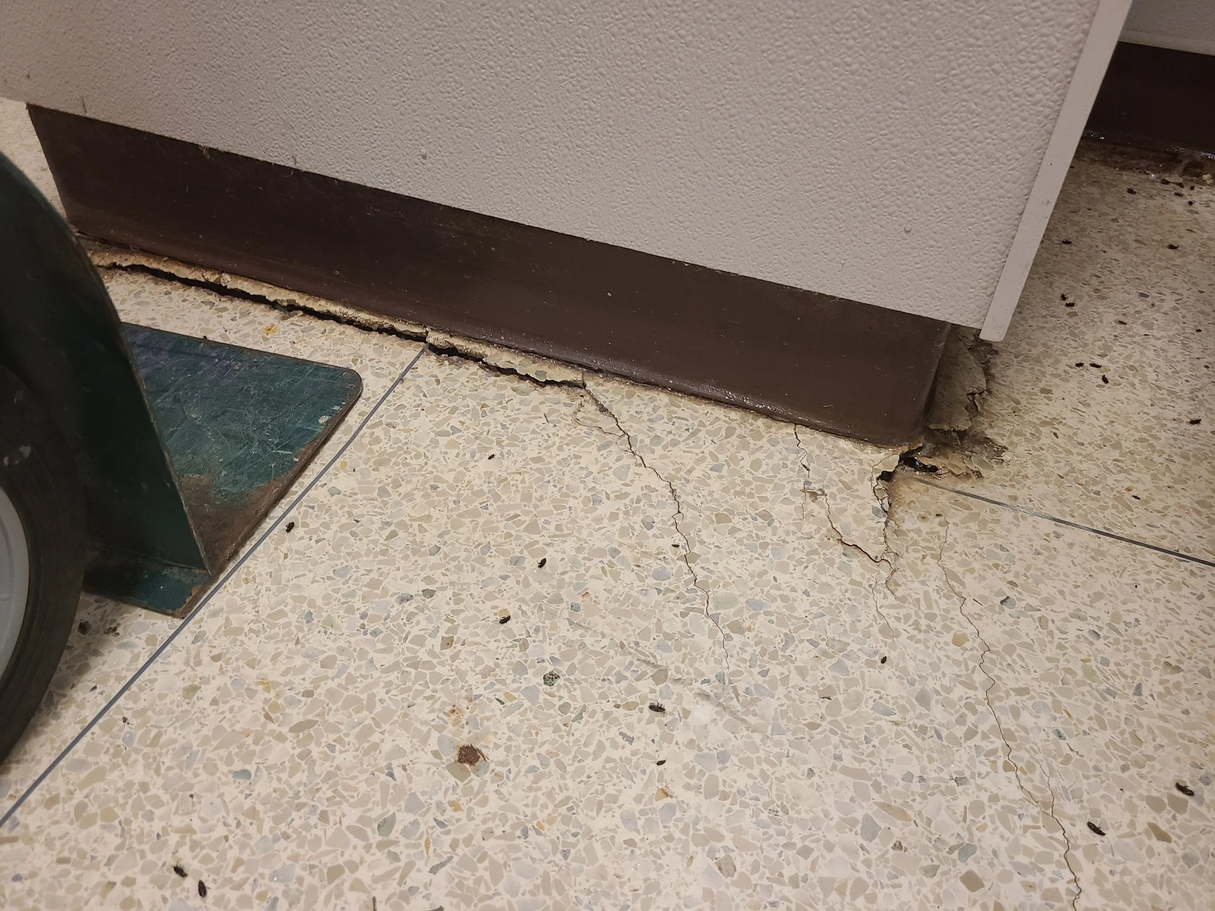 Close-up of a damaged floor with cracked tile and chipped baseboard at the bottom of a wall.