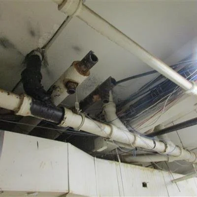 Ceiling pipes and plumbing fixtures, some with leaks and rust in need of repair.