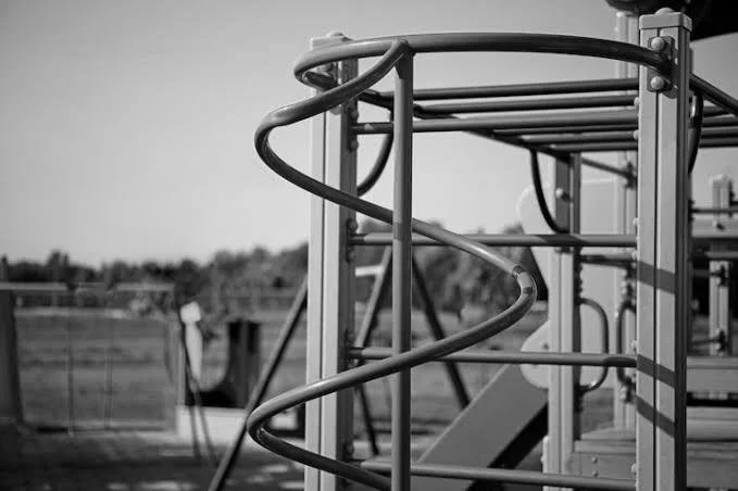 Black and white photo of a playground structure with a spiral slide in the foreground and a slide in the background.