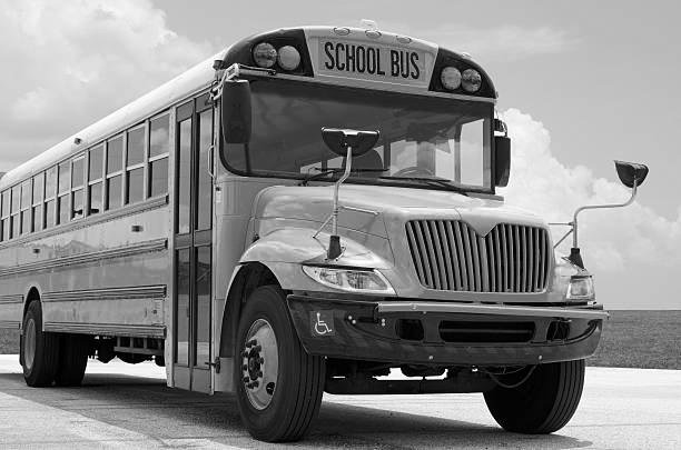 Black and white image of a school bus parked outdoors with a cloudy sky in the background.