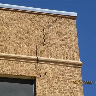 Crack in the brick exterior wall of a building near a window and a horizontal metal strip.