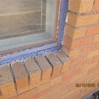Close-up of a brick building corner with a window and a ledge showing some mortar chipping.