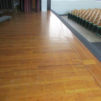 Empty auditorium with wooden floor and stacked chairs along the side.