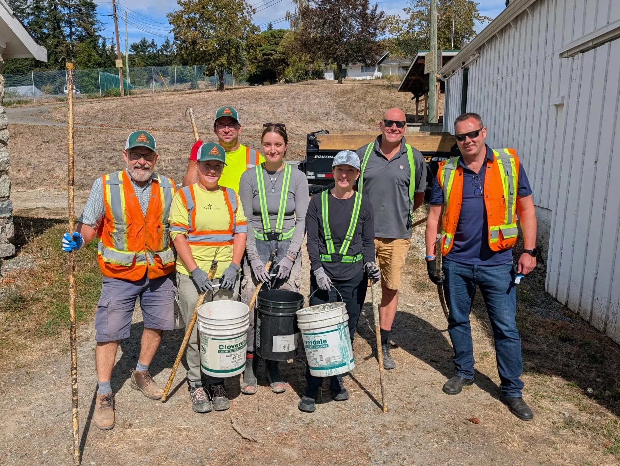 Group of Arbutus Grove team members smiling at photographer, wearing gloves, carrying buckets