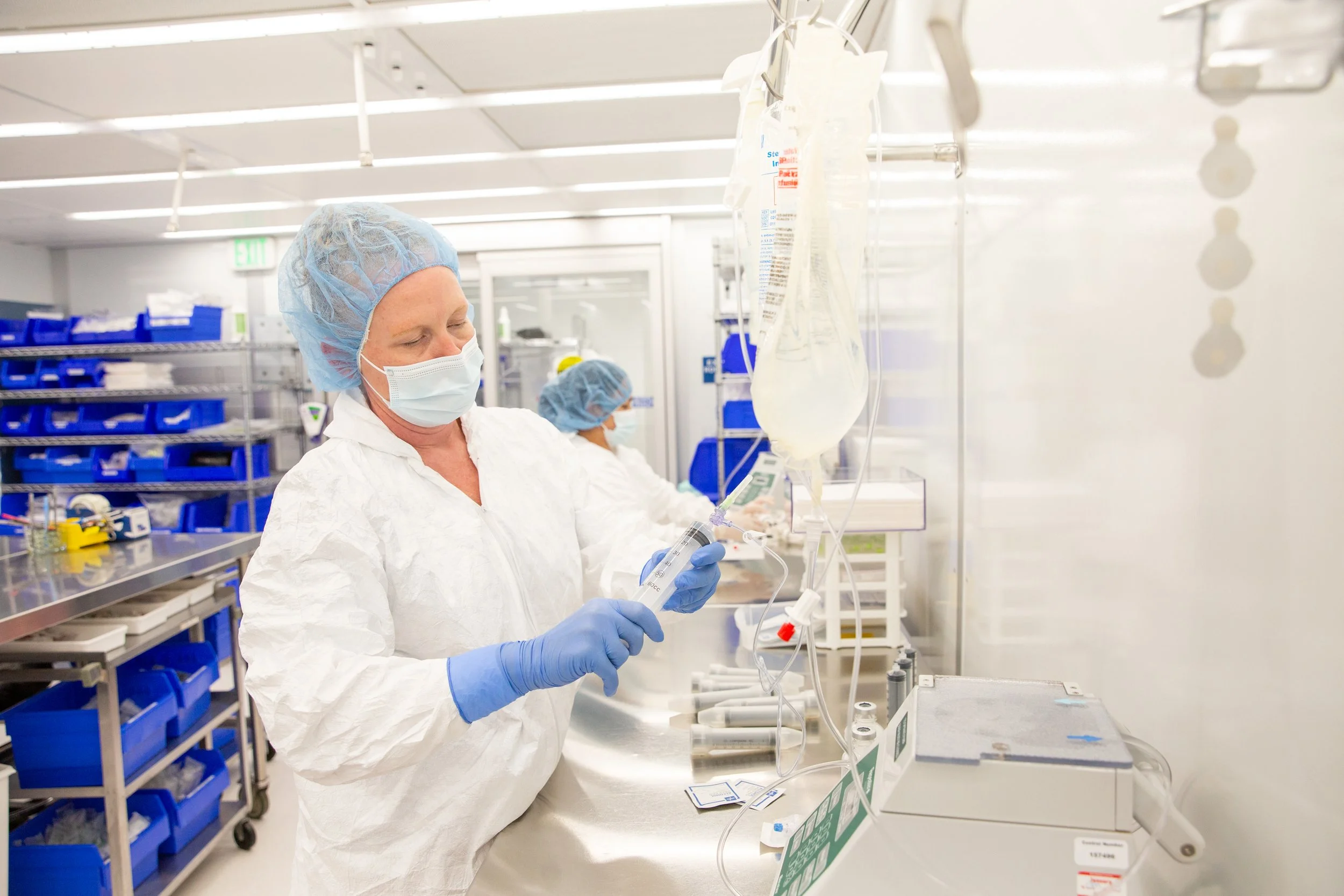 A healthcare worker wearing protective clothing, a face mask, and gloves preparing a syringe in a laboratory setting.