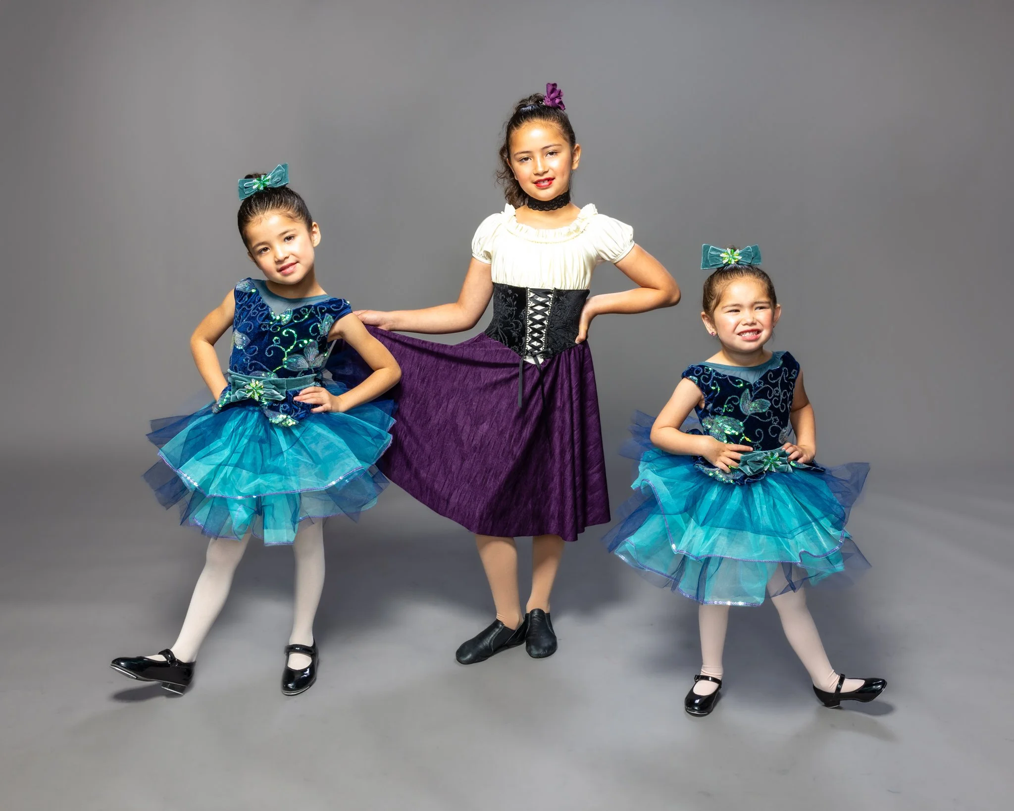 Three young girls in colorful costumes standing against a gray backdrop.