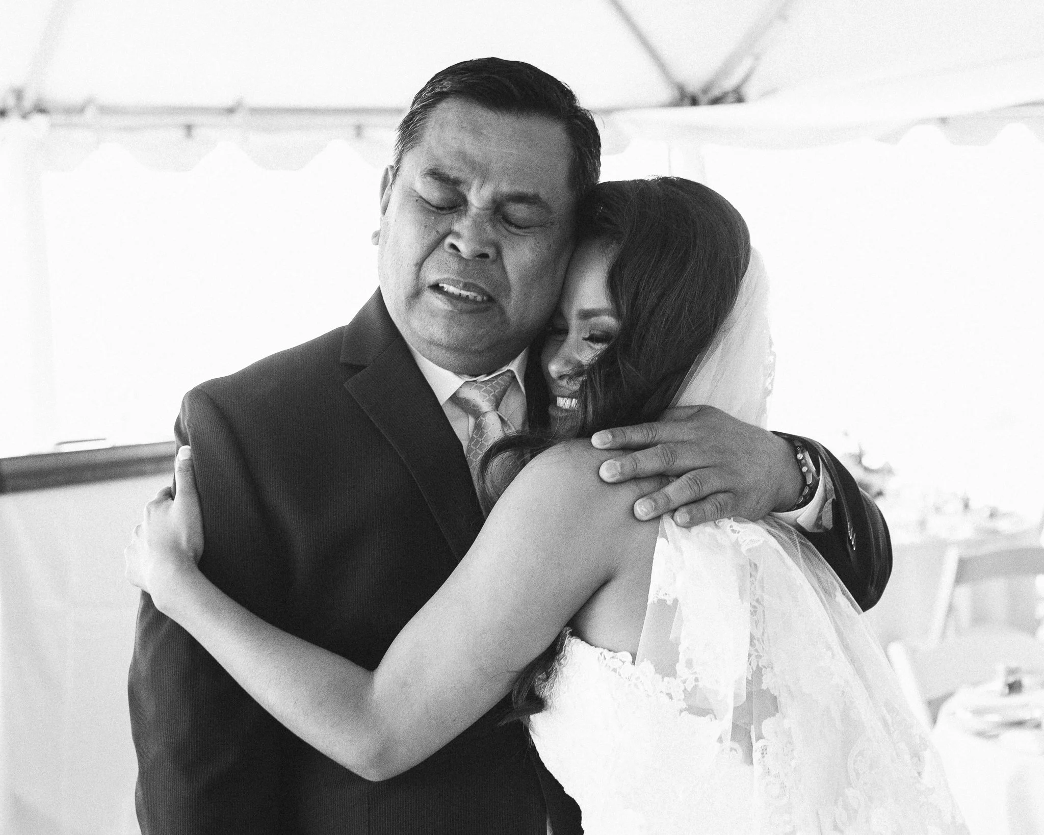 A groom and bride embrace each other during their wedding, with emotional expressions on their faces, in a black-and-white photo.