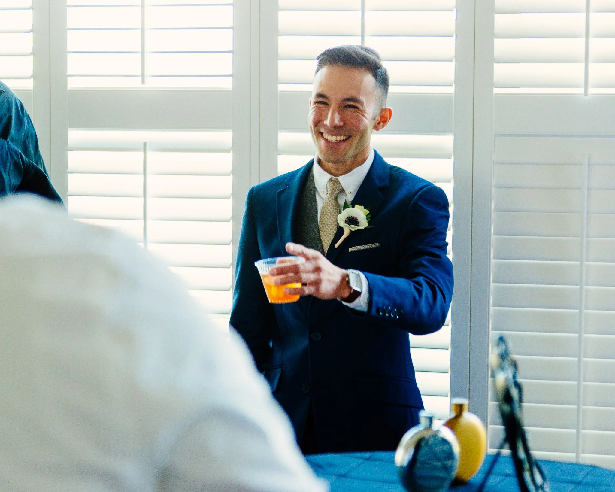 A man in a blue suit and tie holding a plastic cup of beer at a social gathering, smiling.