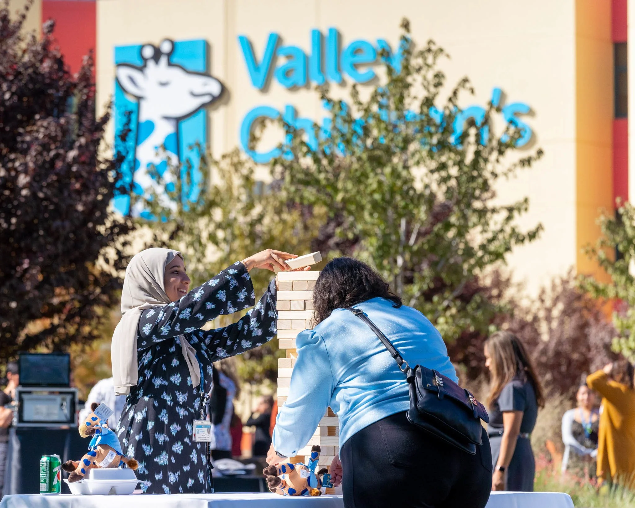 Two women are playing a giant outdoor Jenga game at Valley Children's event, with the Valley Children's logo in the background.