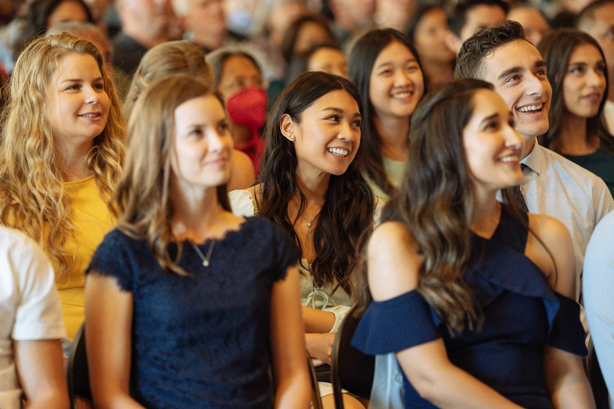 Group of smiling young adults sitting in an audience at an event.